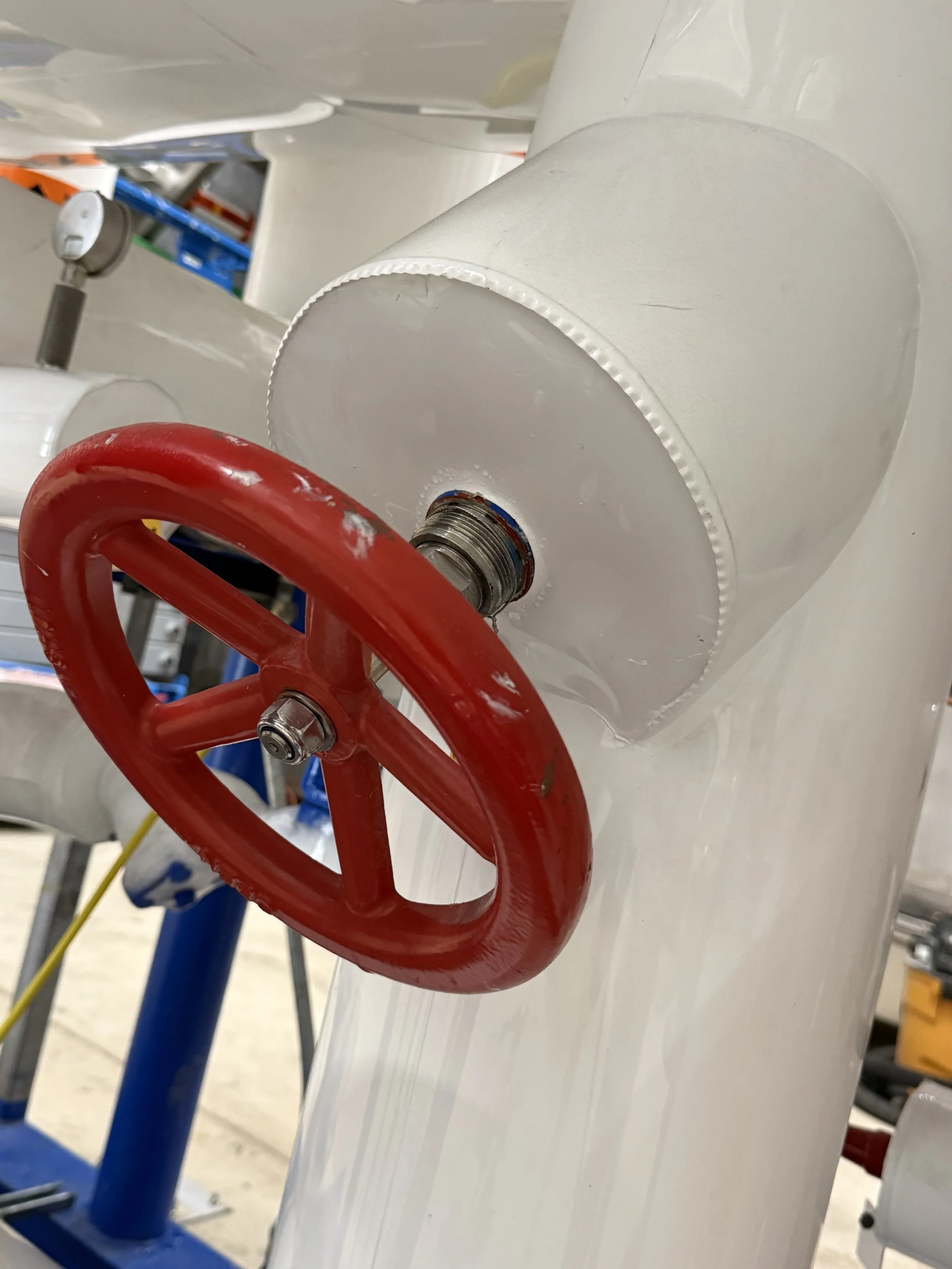 Close-up of a red valve handle attached to a white pipe in an industrial or mechanical setting.