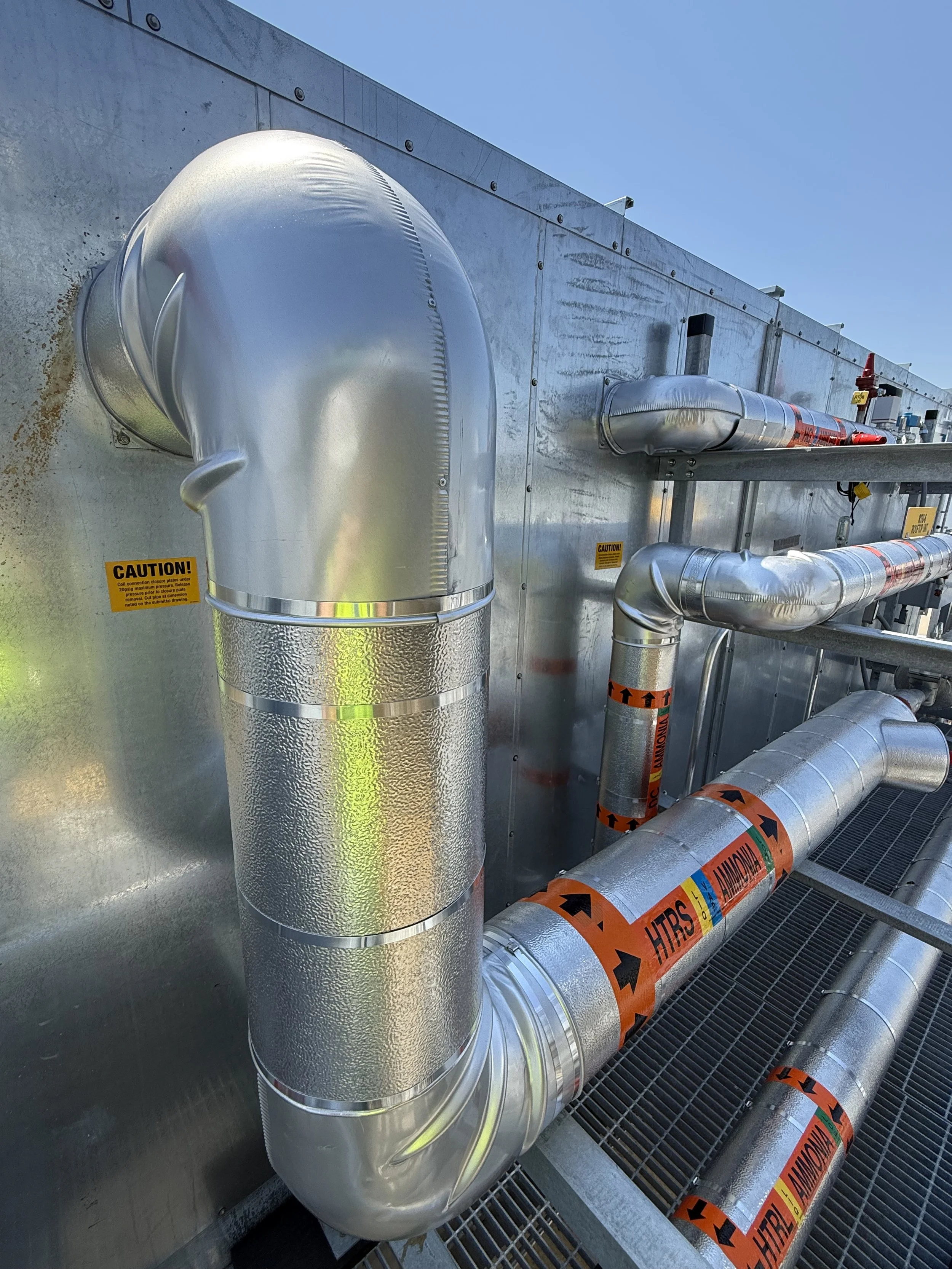 Pipes and ducts on an industrial rooftop with caution and hazard warning labels.
