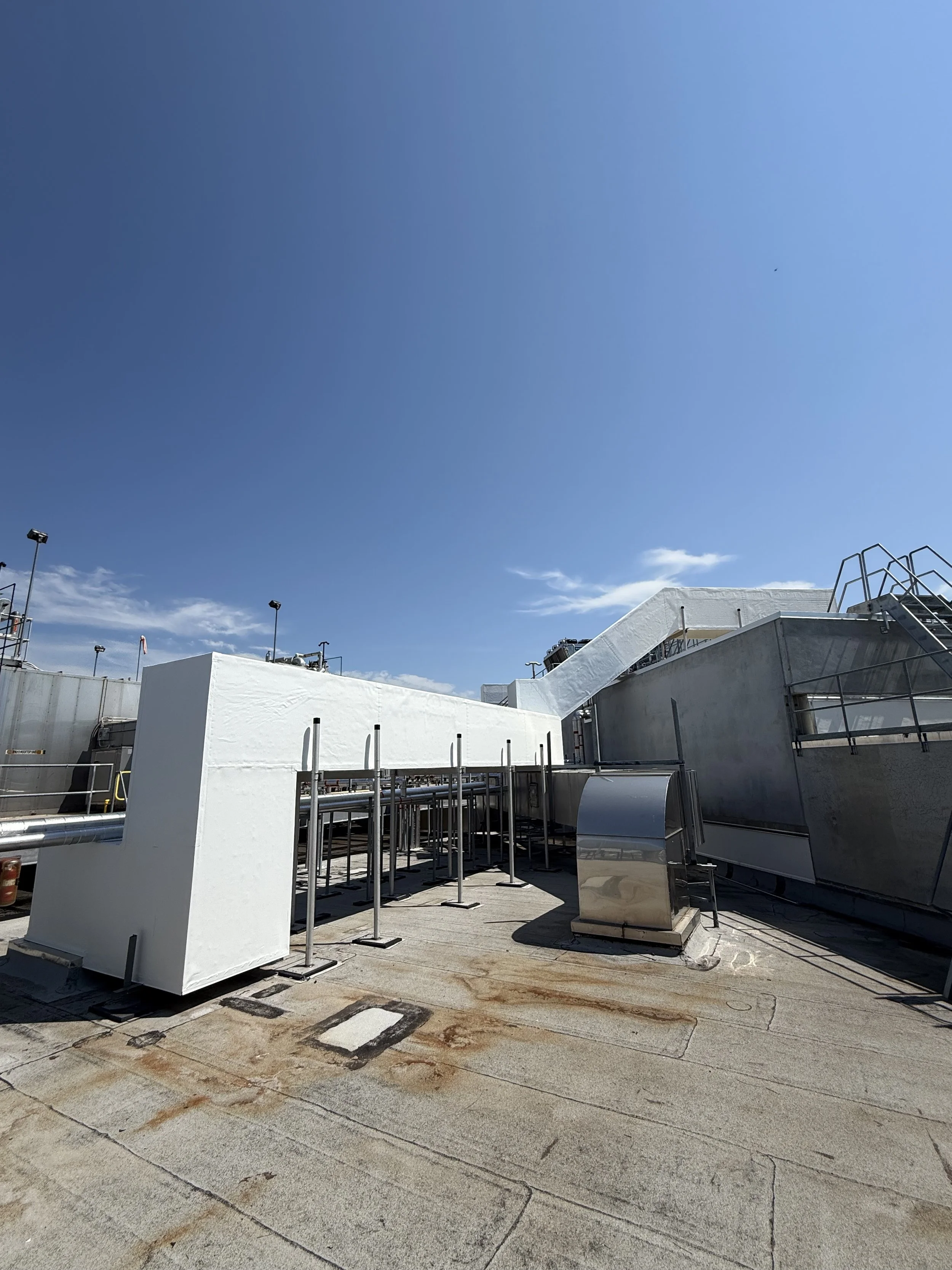Rooftop area with white structures, piping, and equipment under a clear blue sky with some clouds.