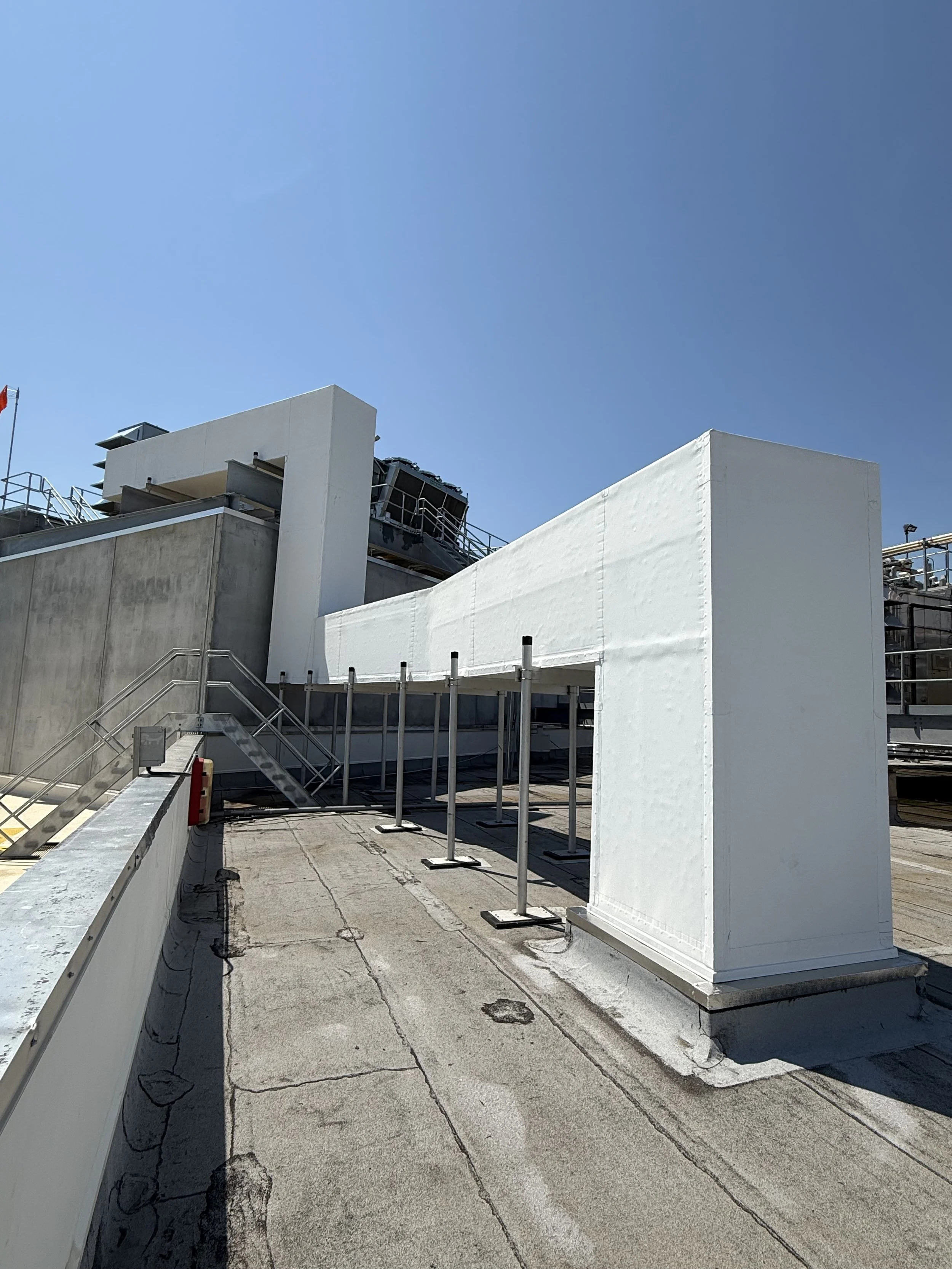 Rooftop area with white structures, metal stairs, and railing under a clear blue sky.