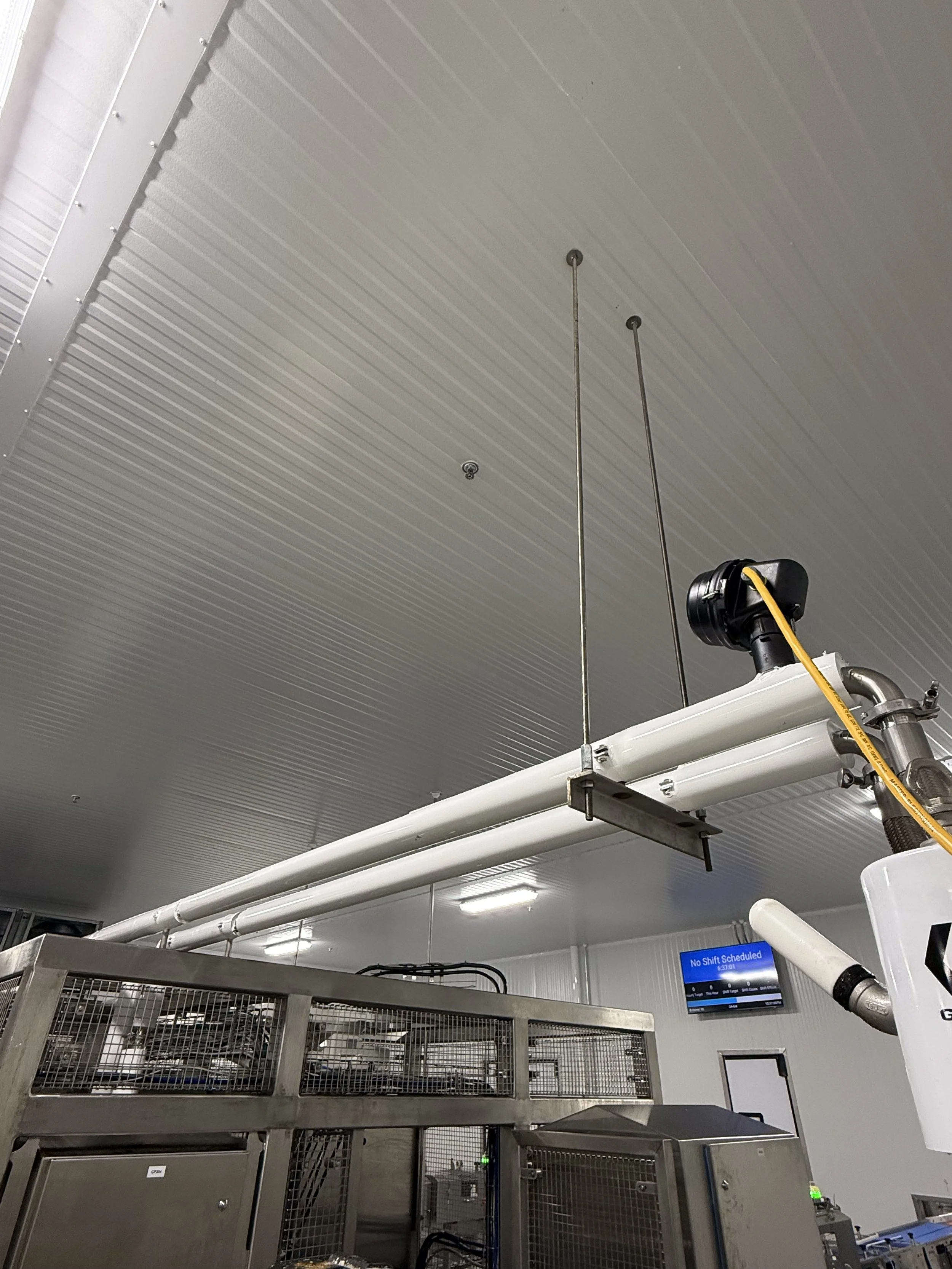 Industrial facility ceiling with pipes, electrical equipment, and a digital display screen.