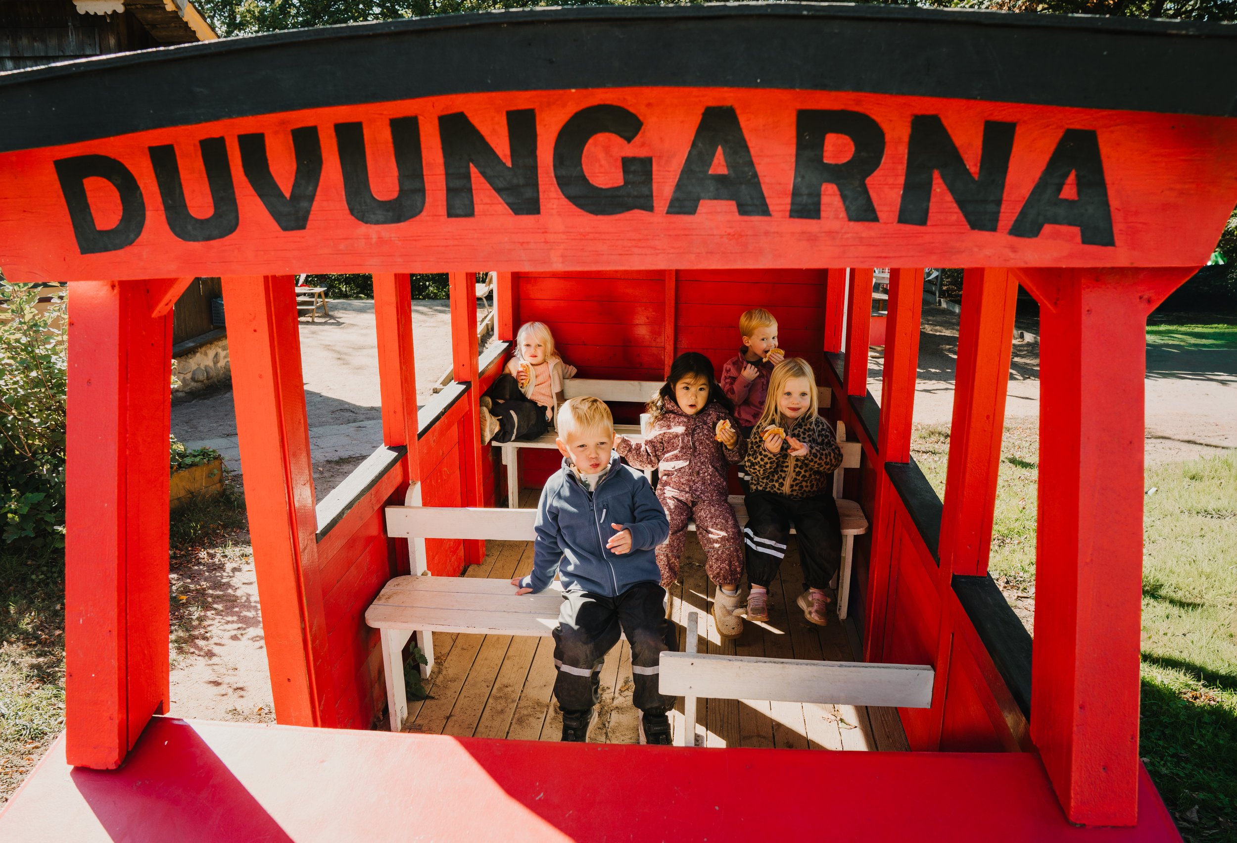 Flera barn som äter glass i en lekstuga i en park.