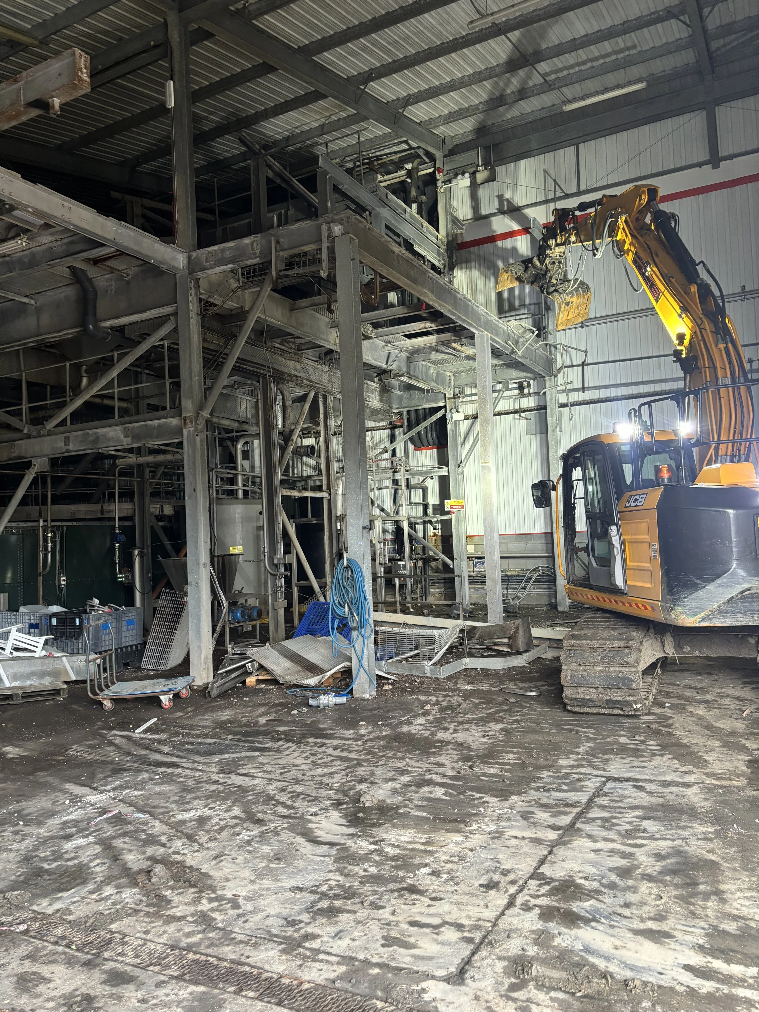 Construction site inside a warehouse with metal framework, heavy machinery, and construction tools, including an excavator and scaffolding.