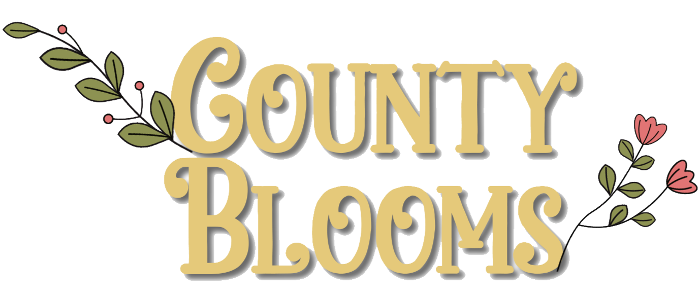 Decorative graphic with the text 'County Blooms' in large, beige letters, accented by pink floral illustrations with green leaves on both sides.