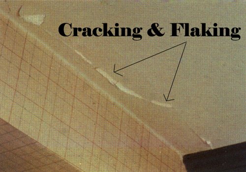 Close-up view of a surface with cracking and flaking paint or coating, with the words 'Cracking & Flaking' labeled and pointing to the damaged area.