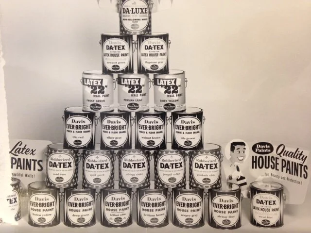 Pyramid of cans of Davis brand latex house paint, including flat wall paint, exterior, and trim, arranged on a display with promotional signage for Davis Paints.