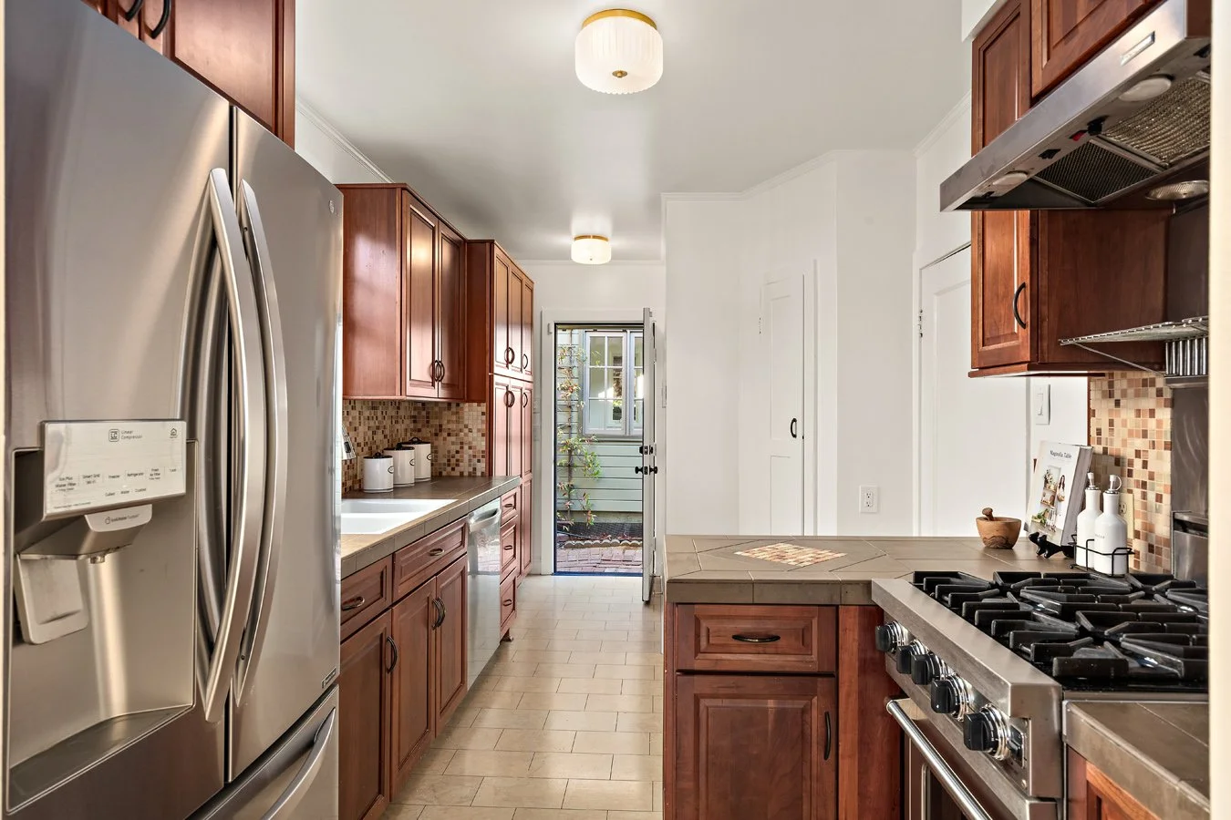 Modern kitchen with wooden cabinets, stainless steel fridge, and a gas stove with tiled backsplash.
