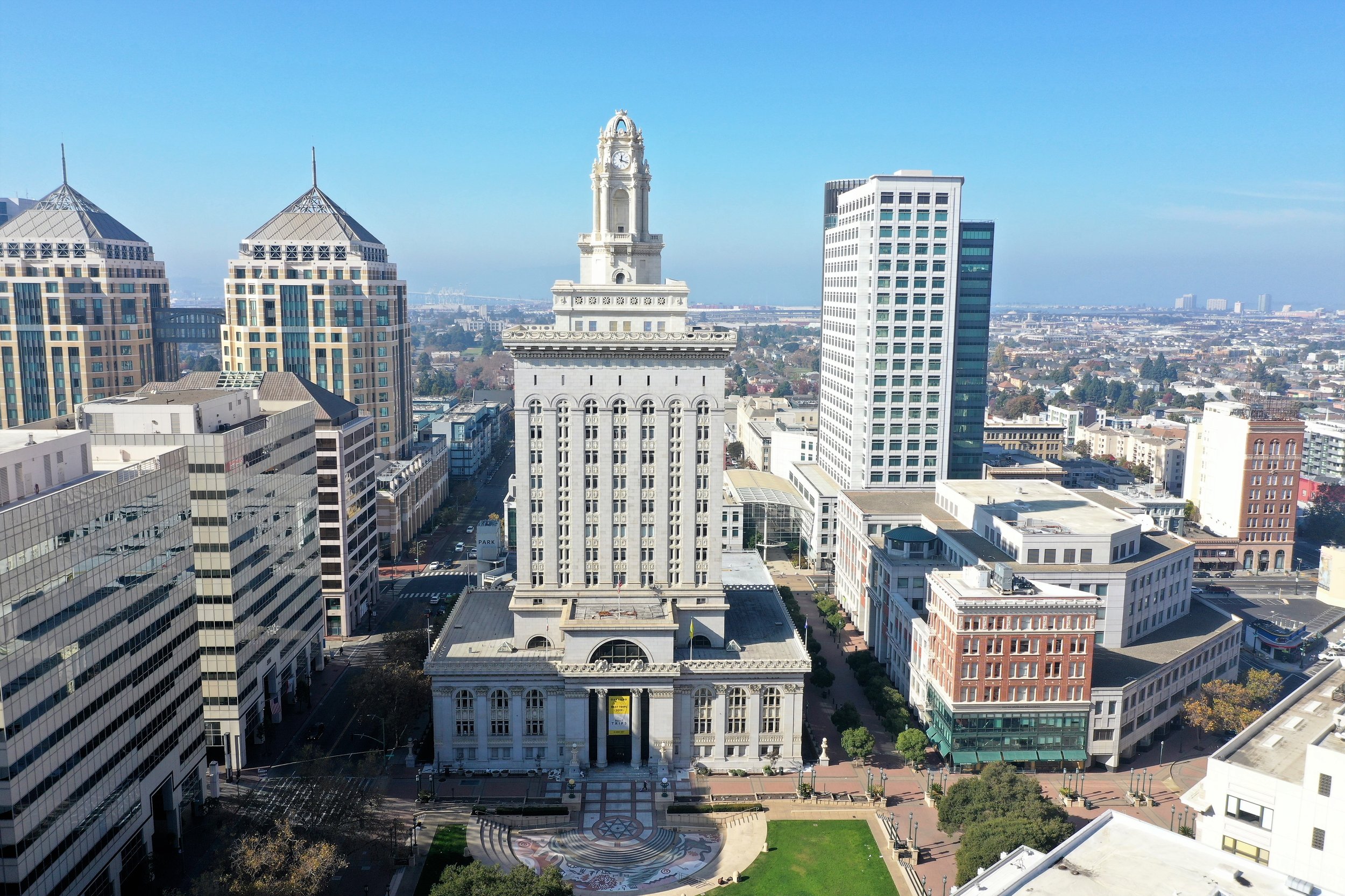 A cityscape with a large white historic building with a clock tower at the center, surrounded by modern high-rise office buildings under a clear blue sky.
