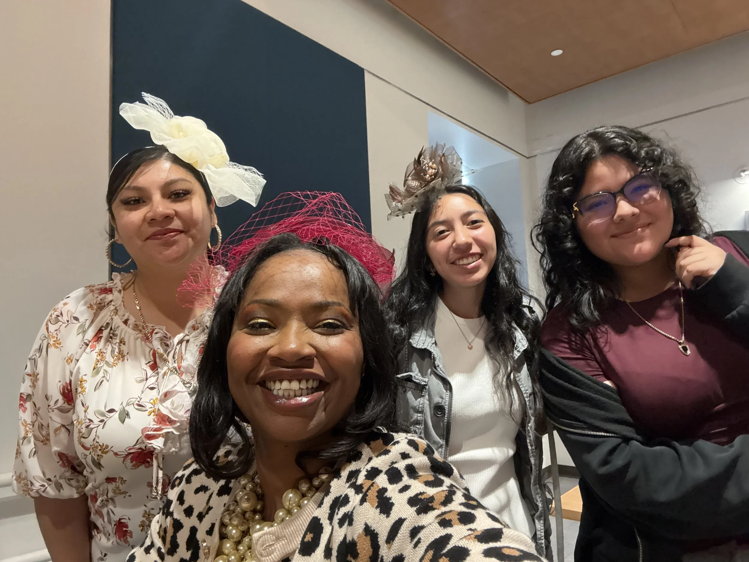 Group of women smiling, some wearing decorative headpieces and accessories, gathered indoors for a celebration or event.