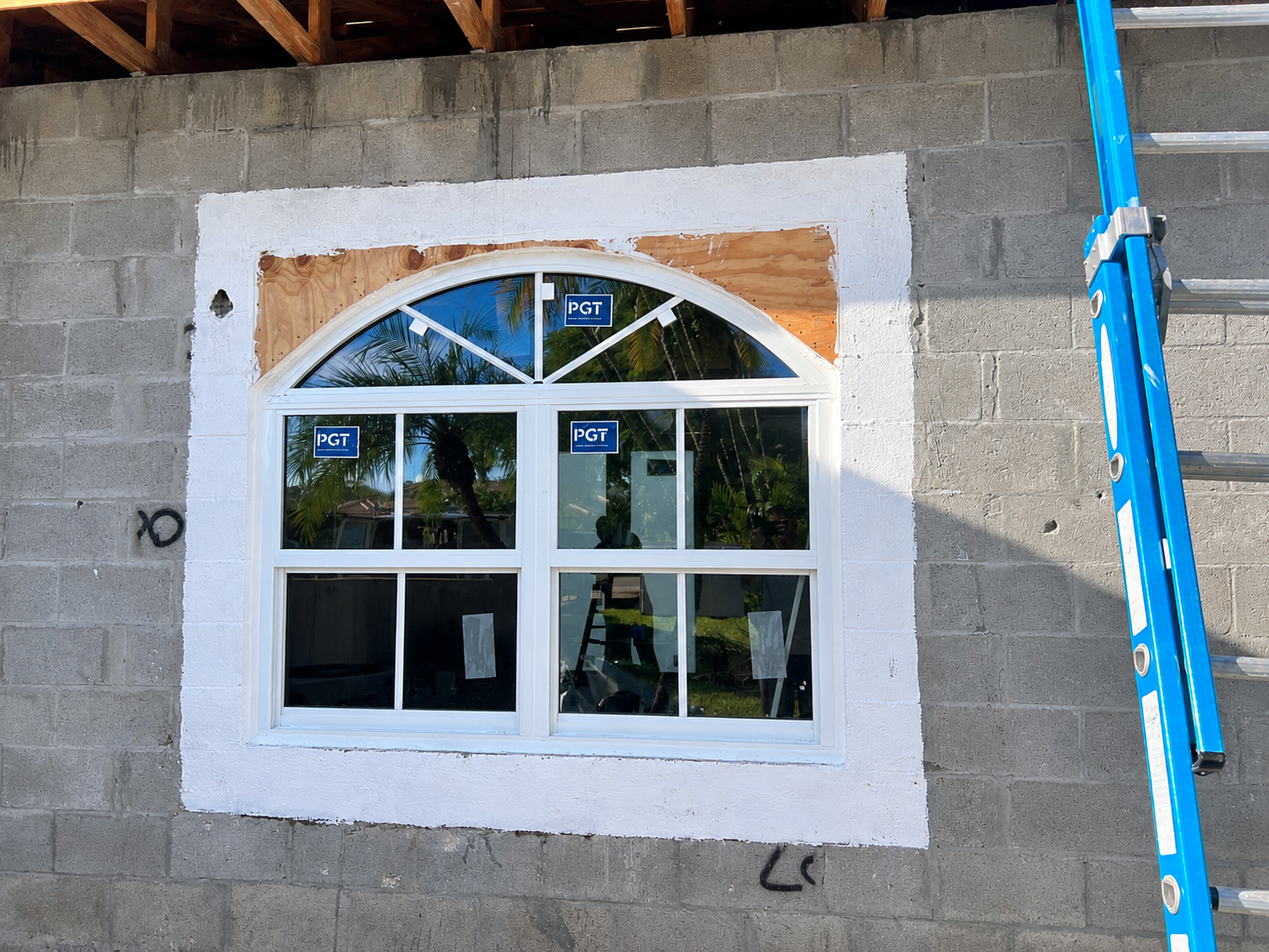 A white arched window installed in a brick wall under construction, with a ladder on the right side.