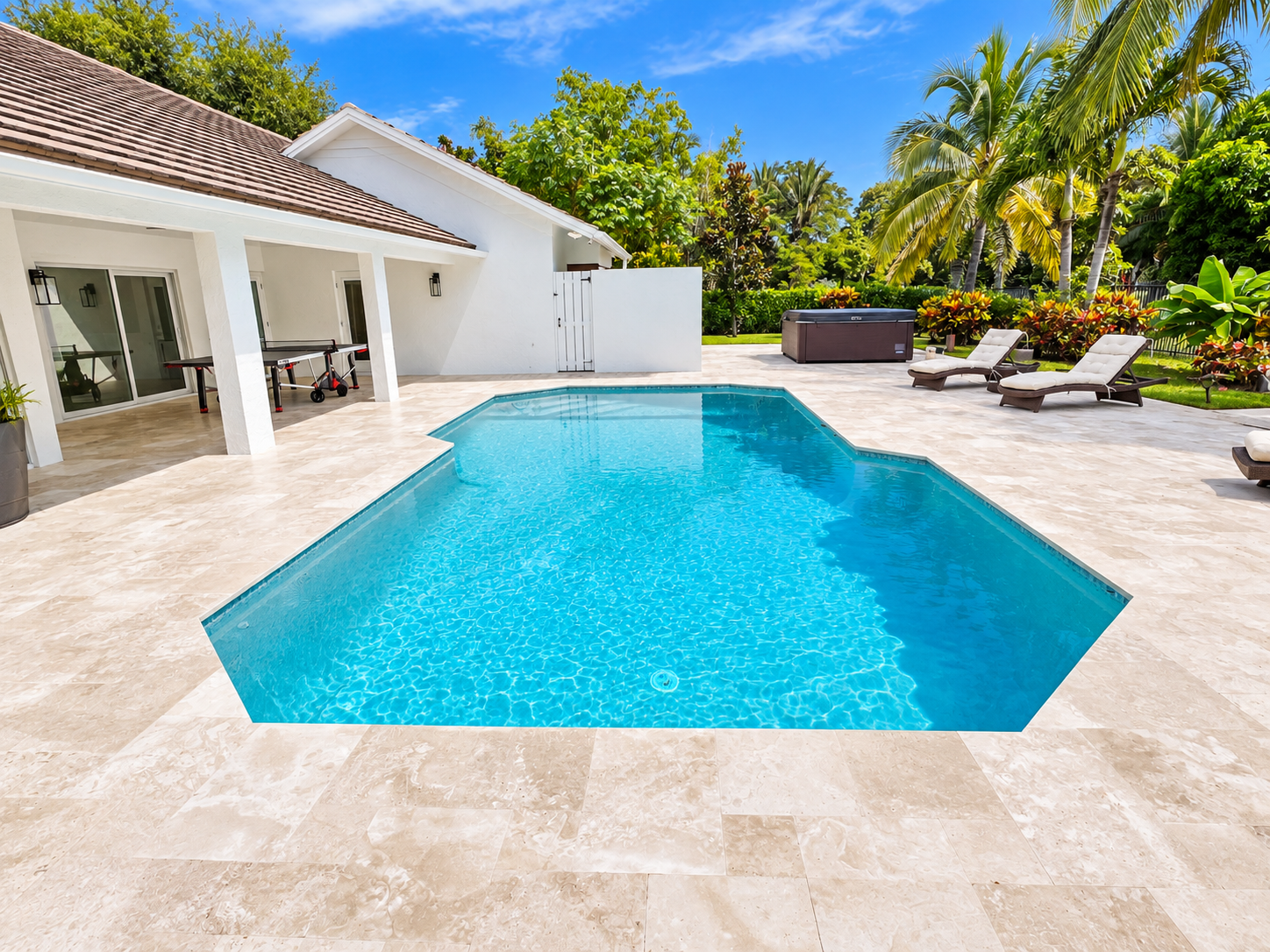 Backyard with a swimming pool, white house, tropical trees, lounge chairs, hot tub, and blue sky