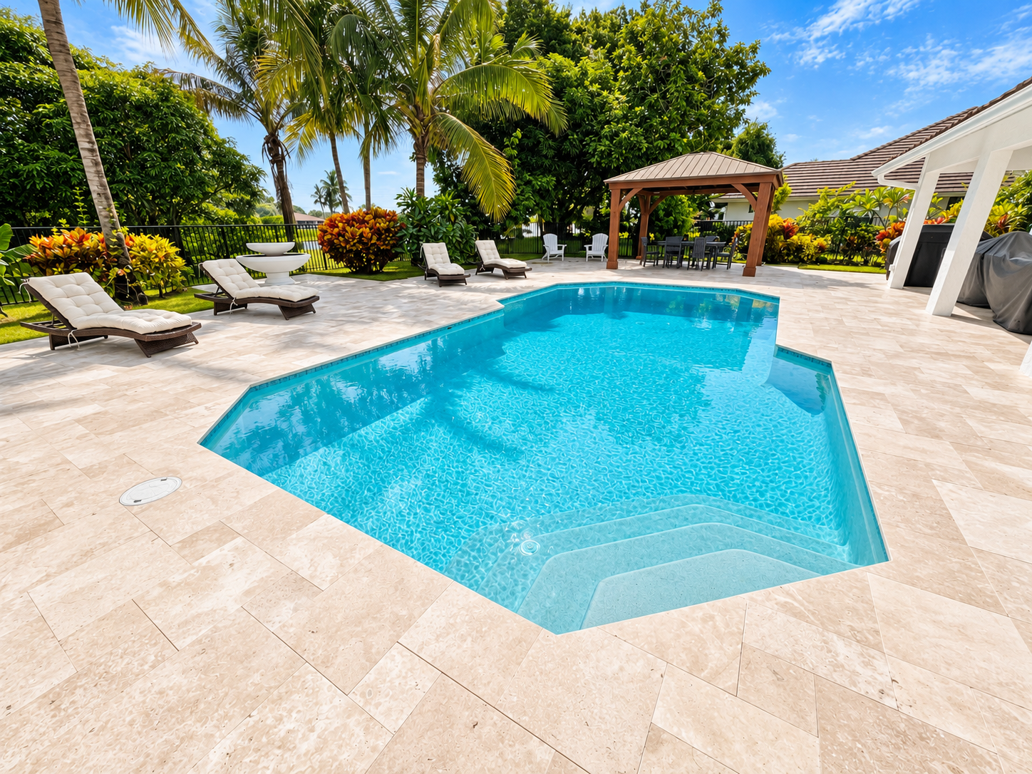 A backyard swimming pool surrounded by lounge chairs, tropical plants, and a gazebo on a sunny day.