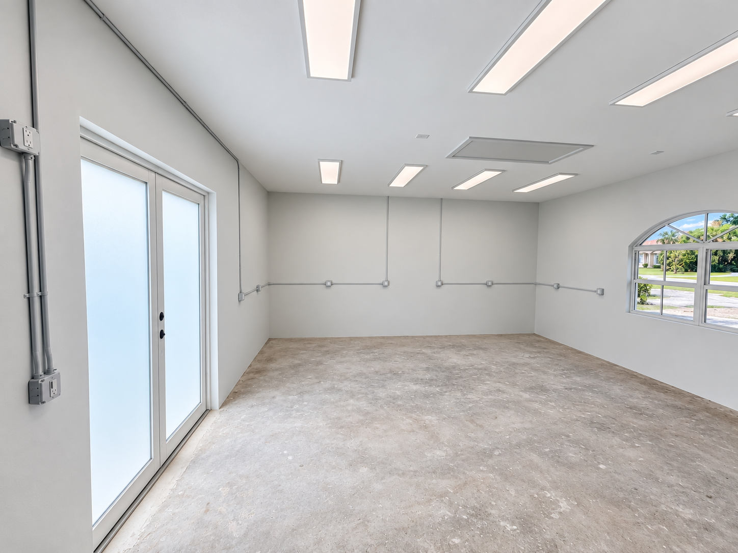 Empty room with white walls, fluorescent ceiling lights, a large window, and double glass doors with frosted glass panels.