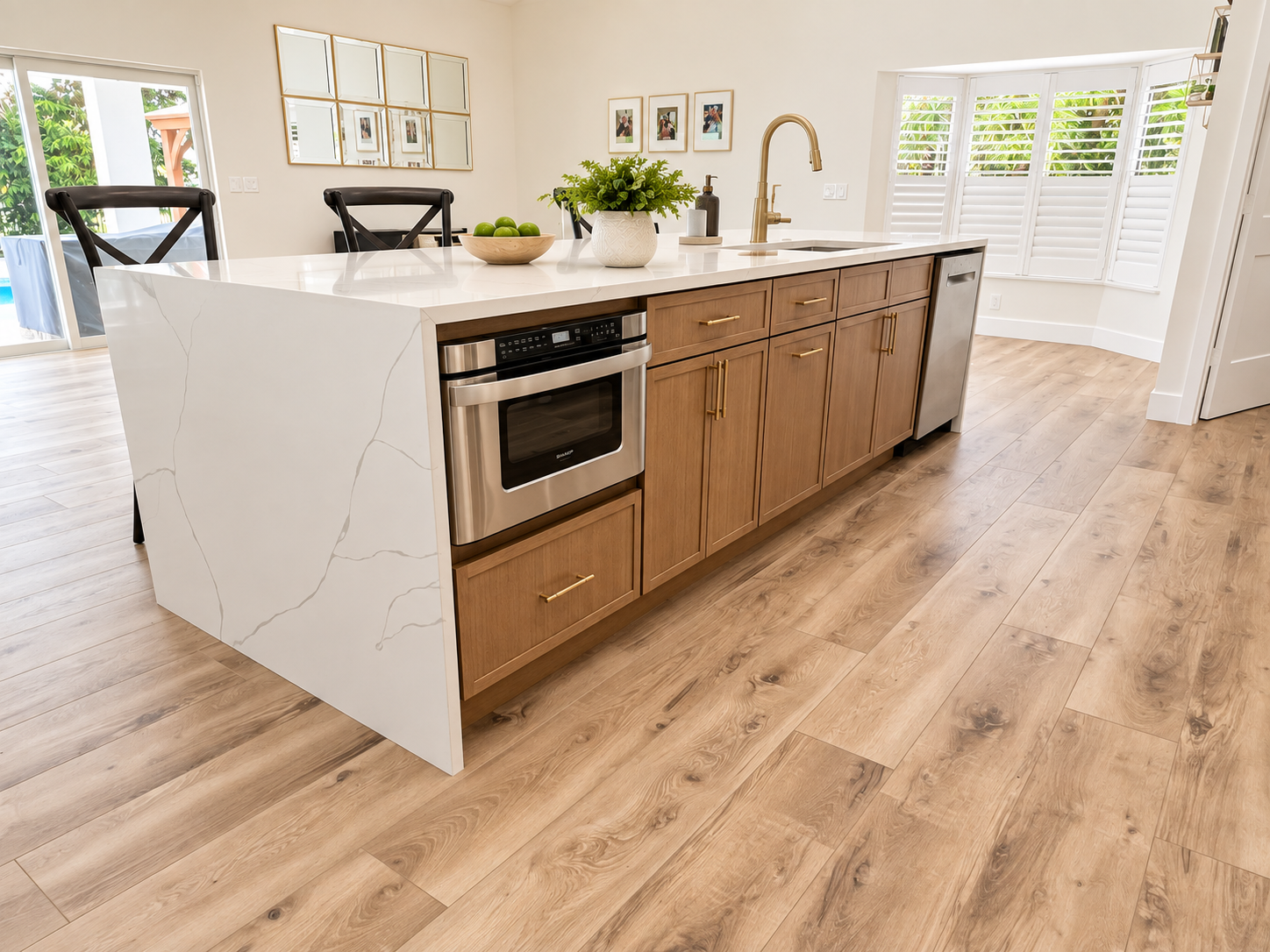 Modern kitchen island with white marble top, wooden cabinets with gold handles, stainless steel oven and dishwasher, and decorative plants and bowls on top.