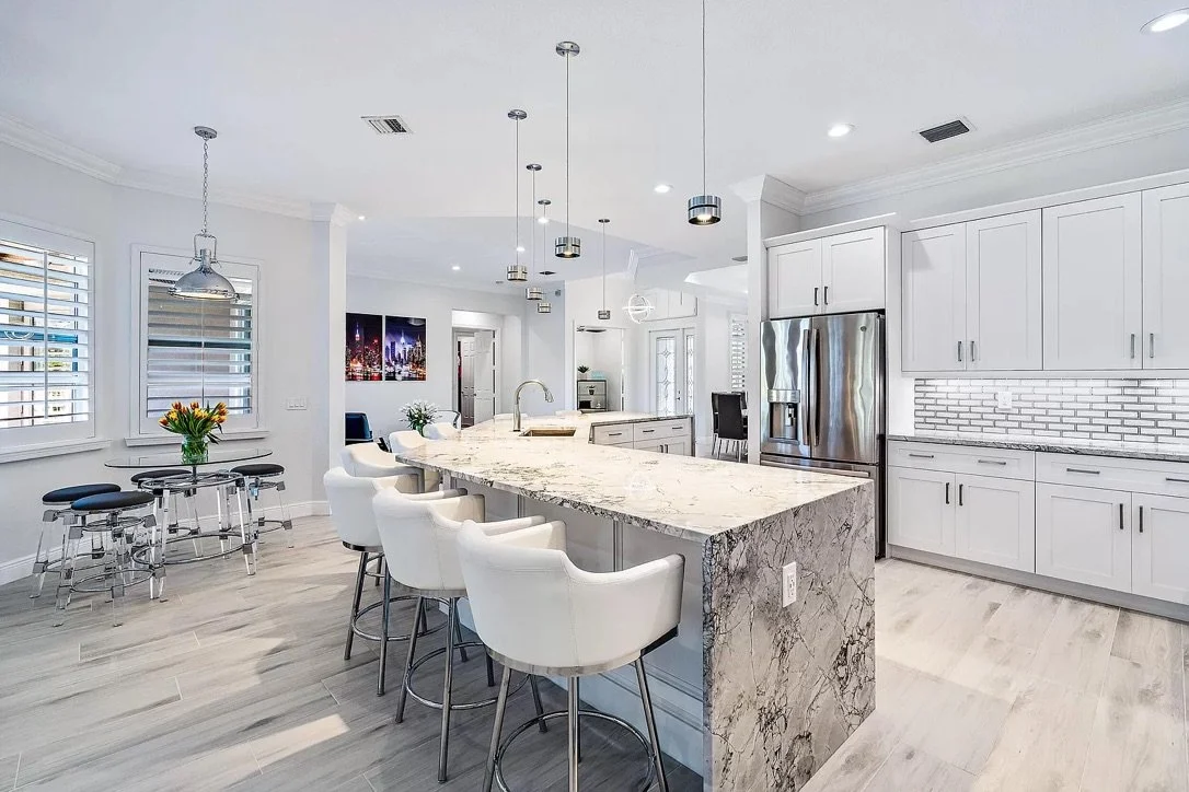 Modern kitchen with white cabinets, a marble island, stainless steel appliances, and a light wood floor.