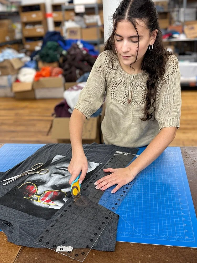 Ruby cutting a graphic T-shirt with a rotary cutter on a blue cutting mat