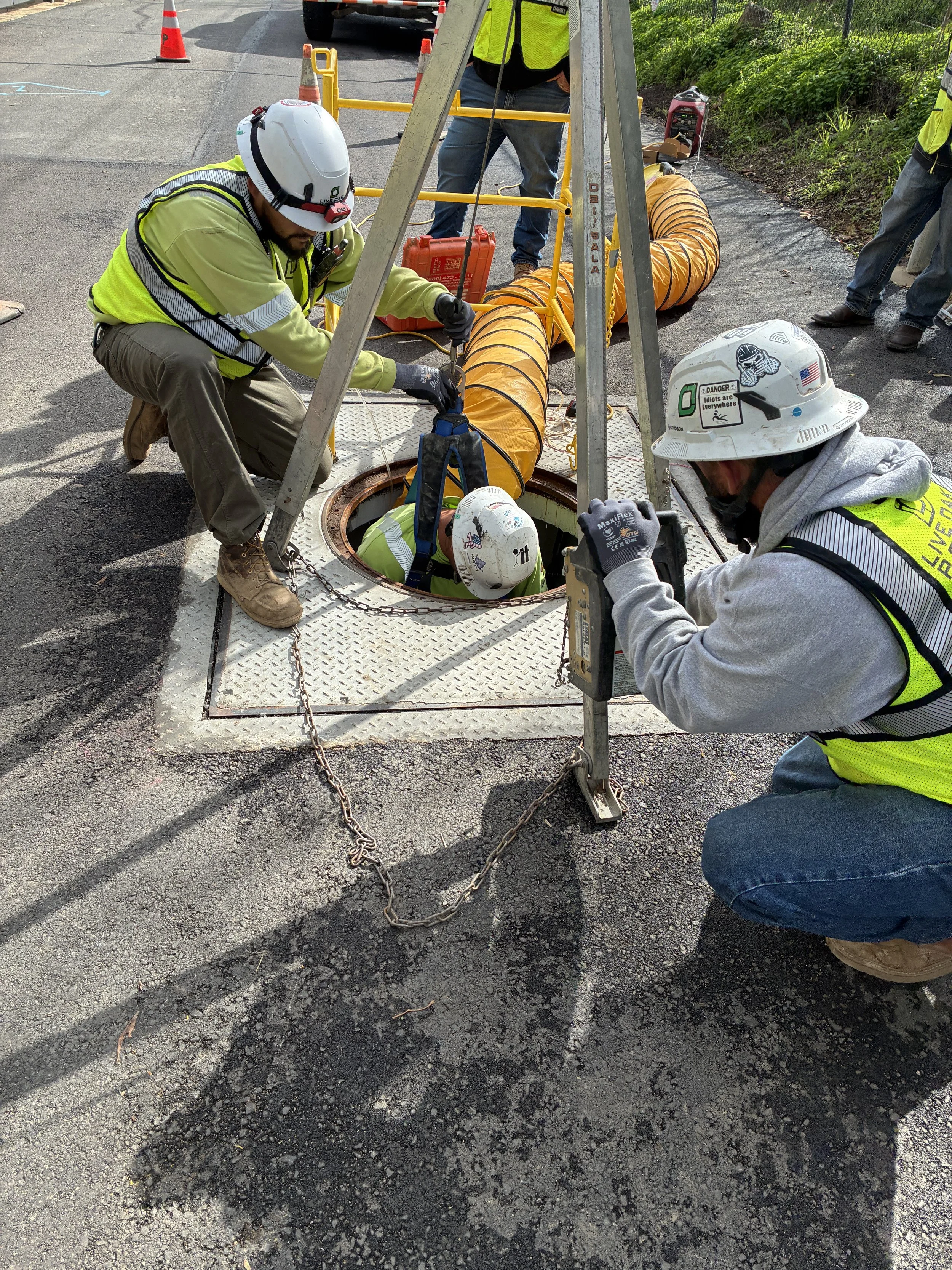 Crew performing underground utility work in a manhole with traffic control in place.