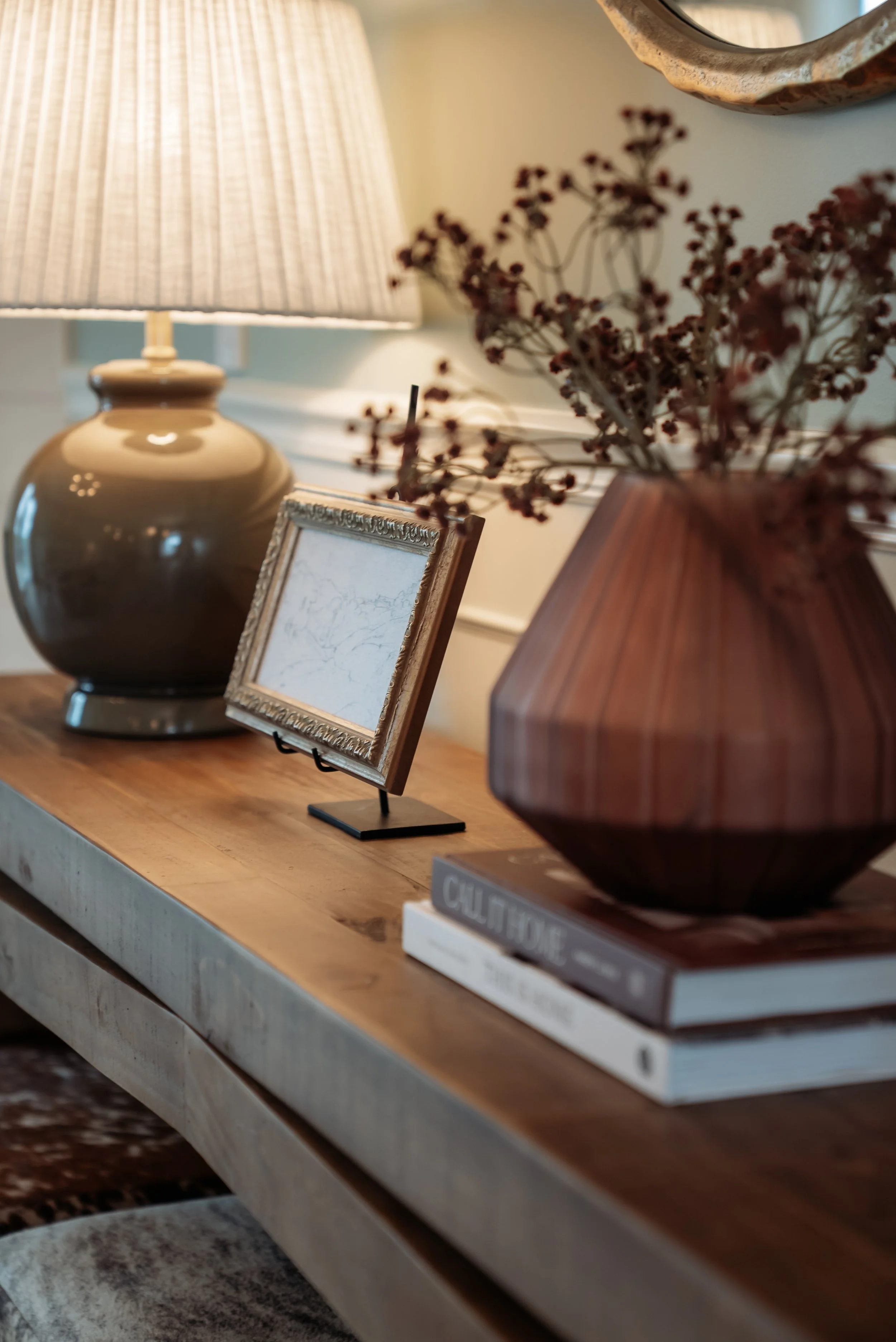 Close-up of a wooden table with vases, picture frame, and books, and a table lamp in the background.