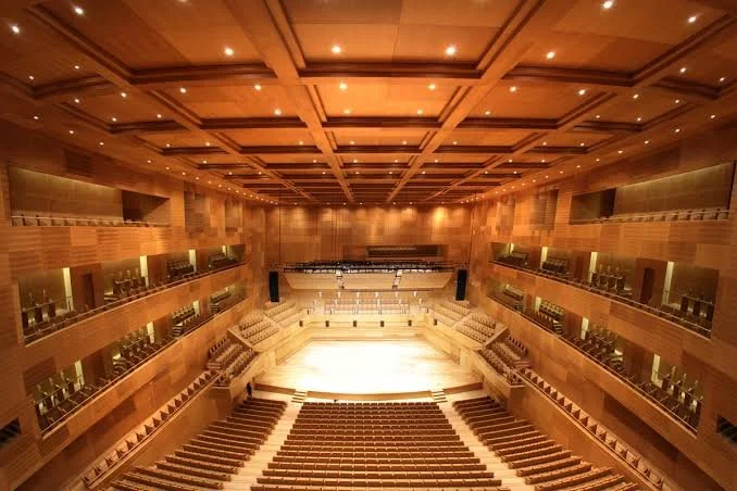 Interior view of a large, ornate concert hall with wooden walls, multiple tiers of balconies, and a stage at the front with seating.