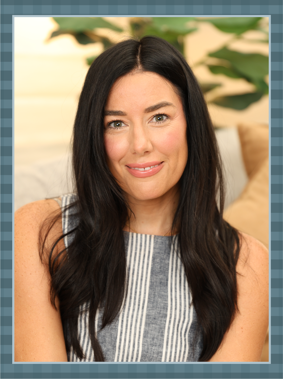Close-up portrait of a woman with long dark hair, smiling, wearing a sleeveless striped top, with a green plant in the background.