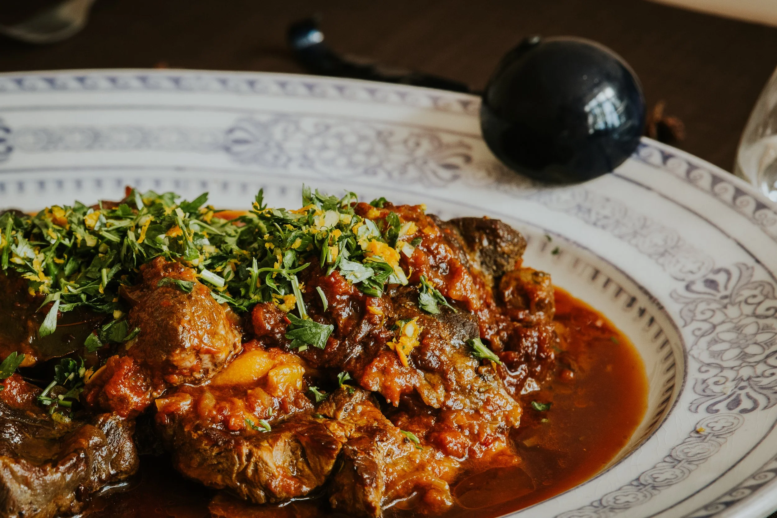 Braised meat dish with rich jus and fresh herbs, restaurant menu photography - Josh Ward Creative