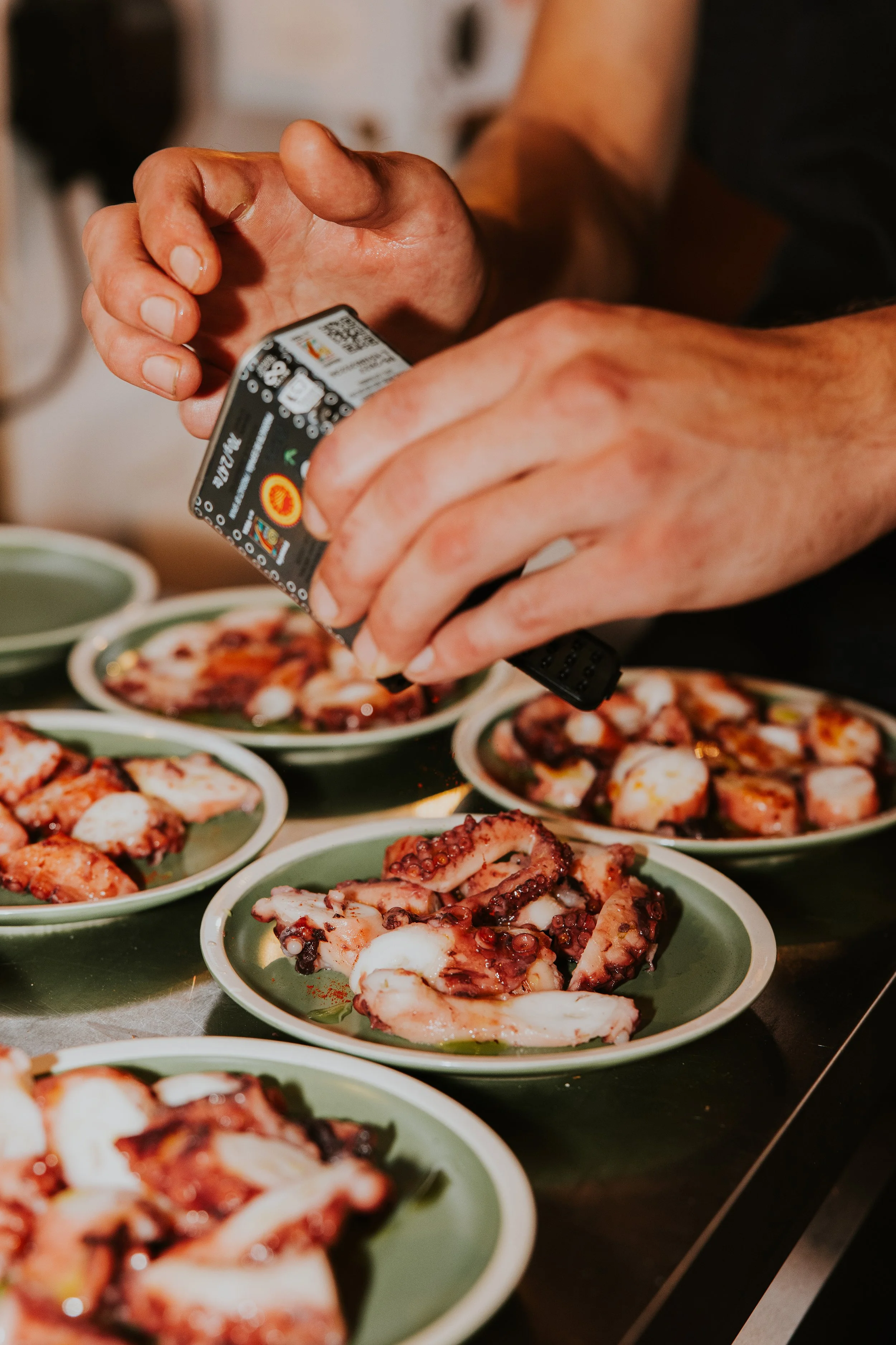 Chef seasoning plated octopus dishes during live kitchen service - Josh Ward Creative