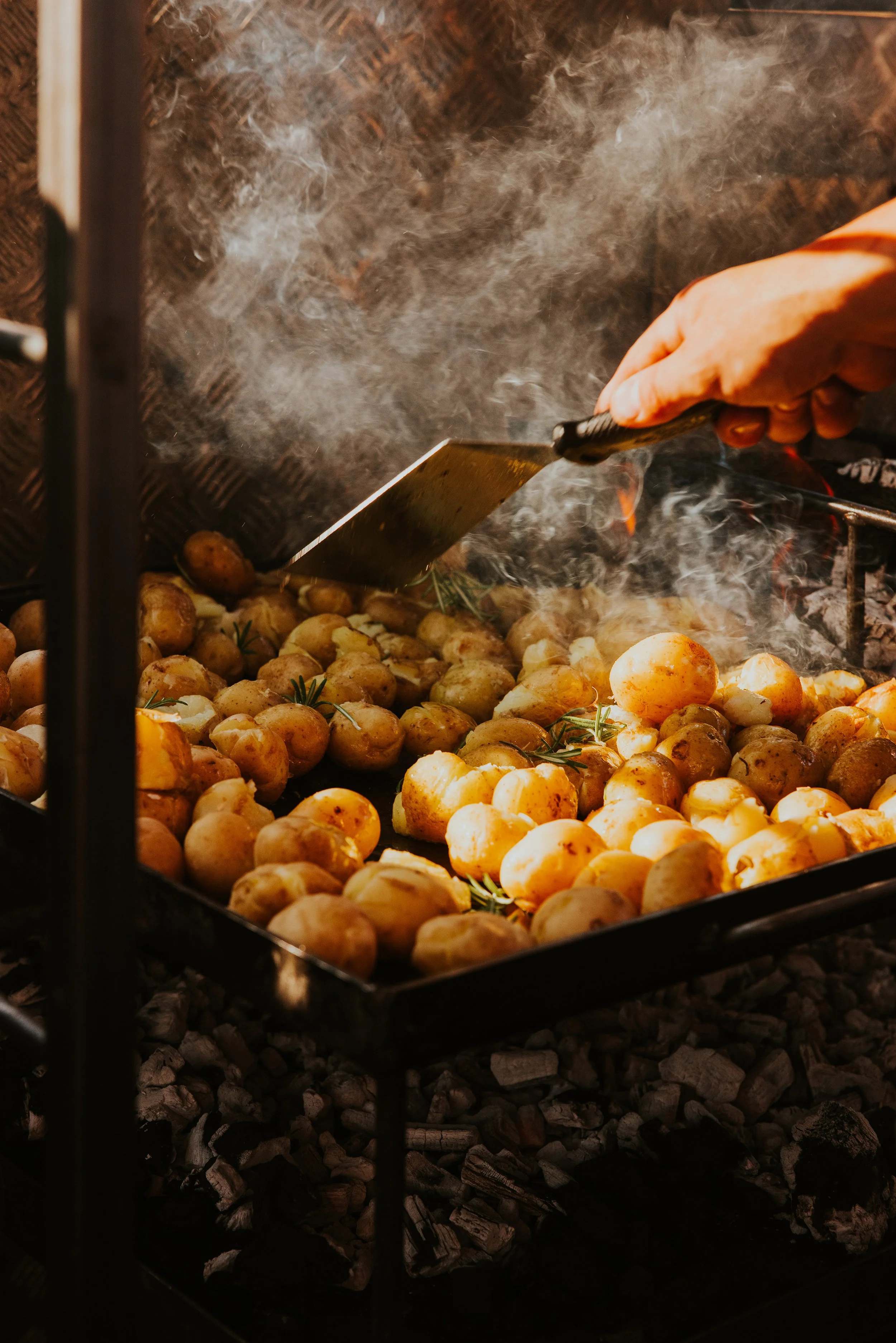 Baby potatoes roasting on live fire flat top grill with smoke and flame - Josh Ward Creative