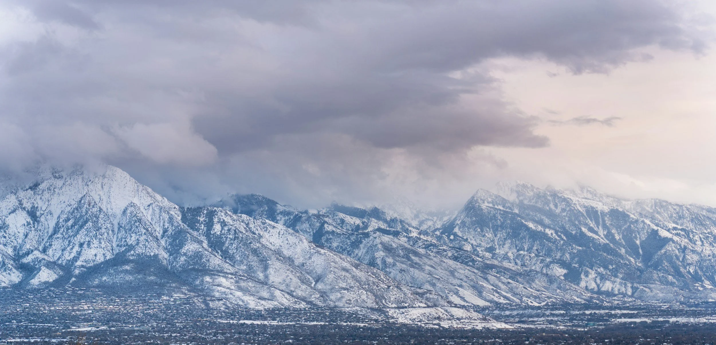 Snow-covered mountains under a cloudy sky with some light breaking through.