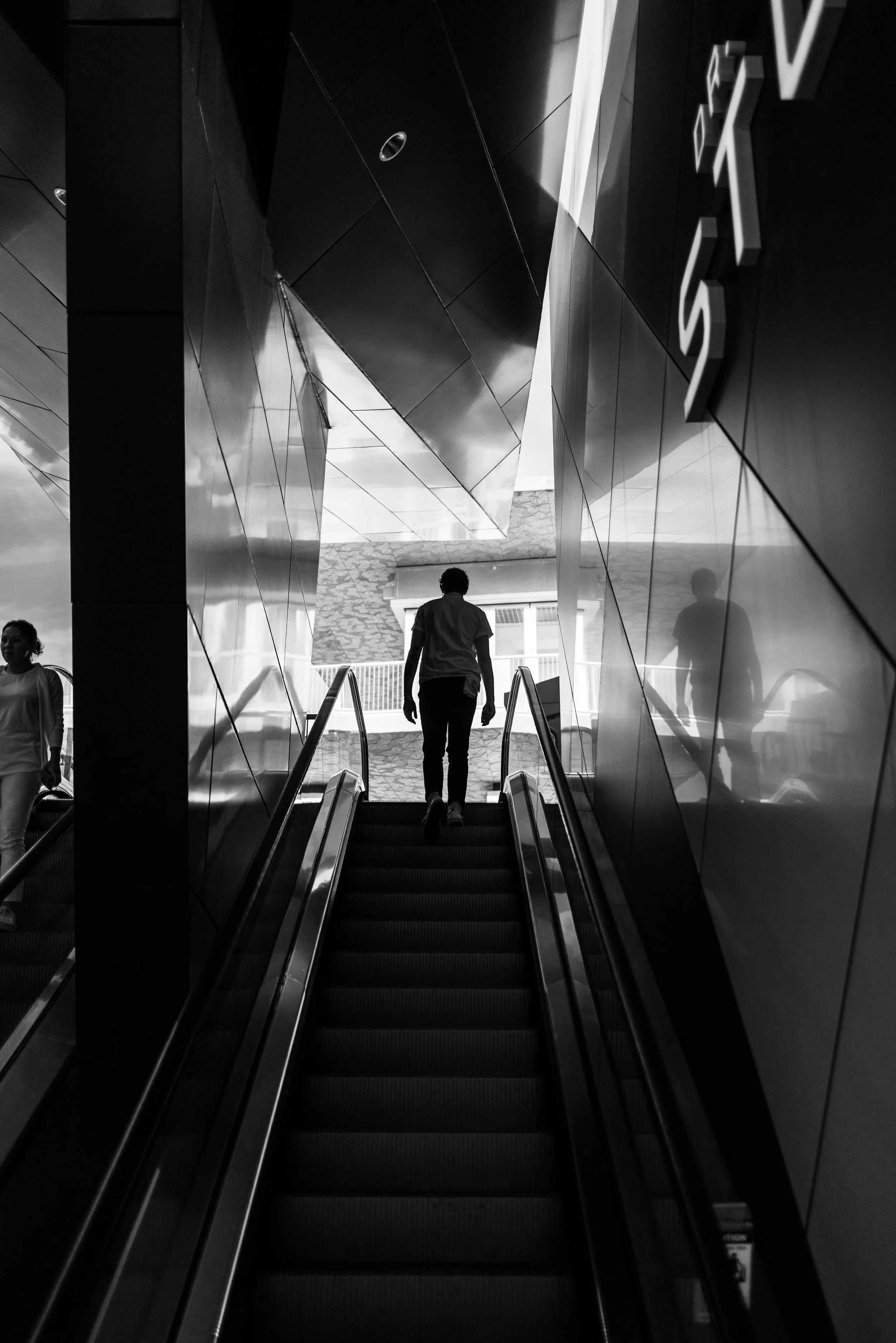 A silhouette of a person moving up an escalator in Miami with his reflections off the metallic walls making for a mysterious picture