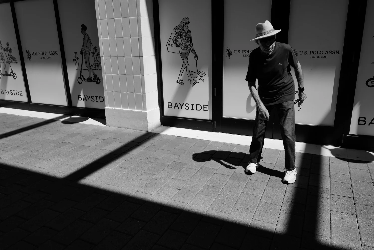 Man in a hat walking past illustrated storefront windows in sunlight and shadow