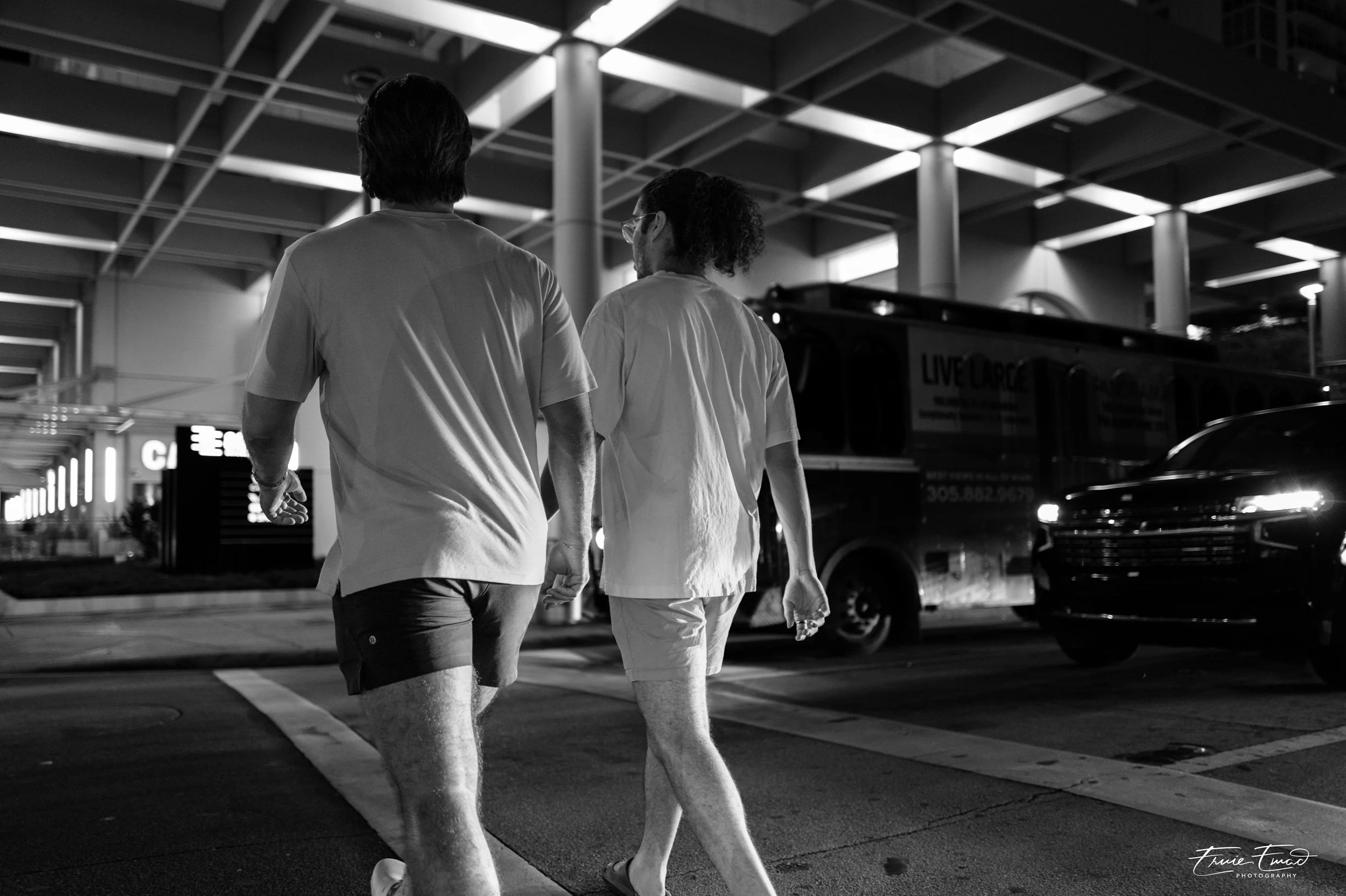 Two people walking hand in hand through a parking lot at night, black and white photo.