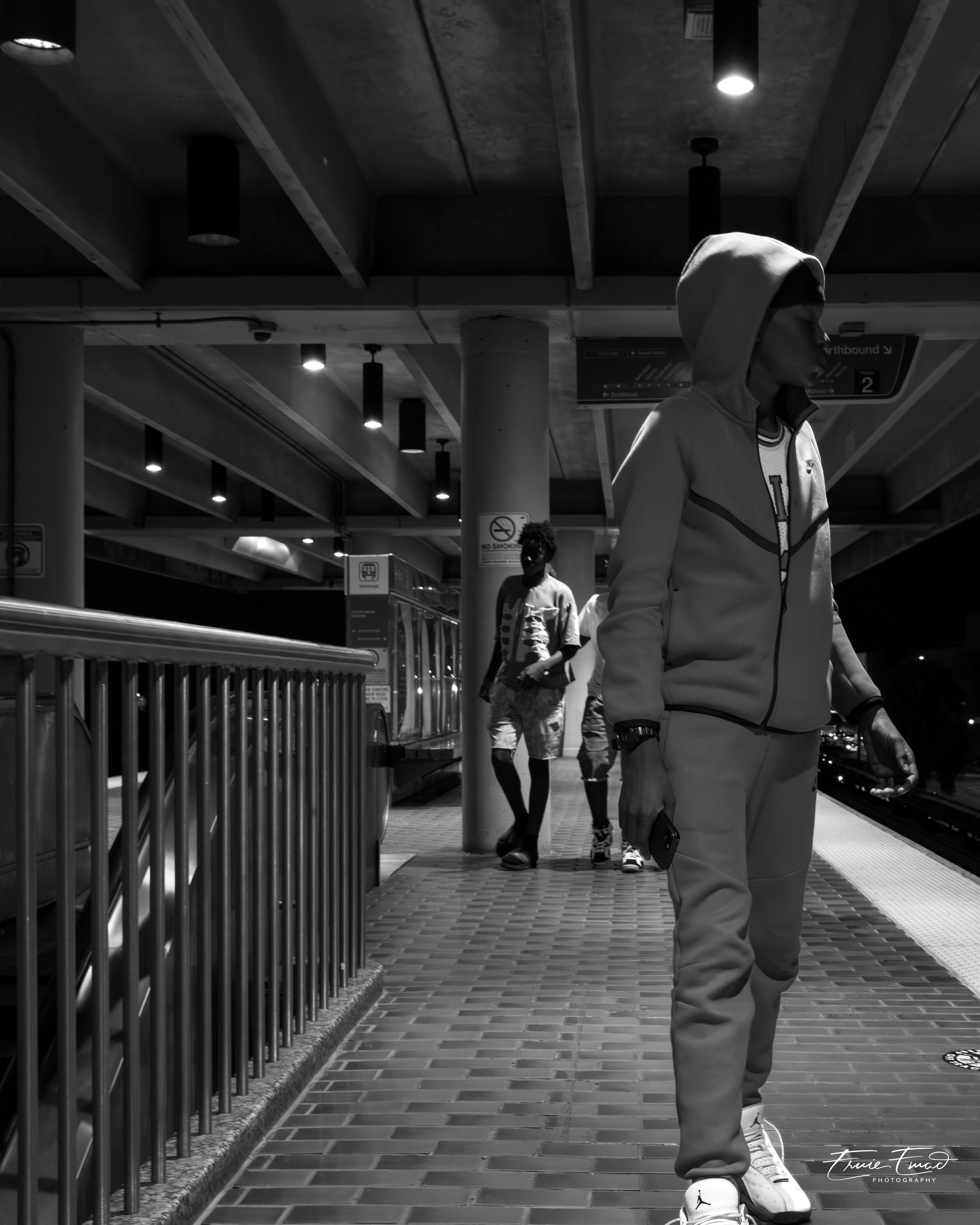 A person wearing a hoodie and walking on a tiled floor in an indoor setting with ceiling lights and columns.