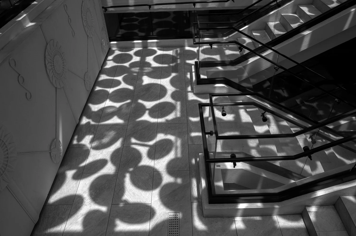 Black-and-white staircase photograph with circular shadows across a tiled floor