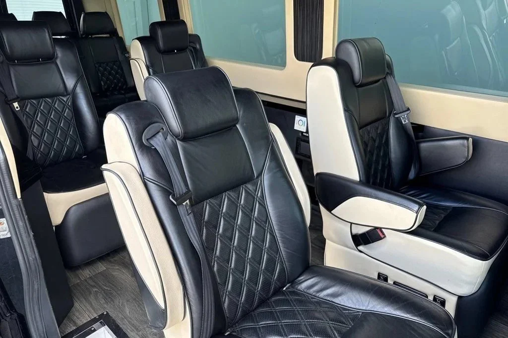 Interior of a luxury passenger van showing black leather seats with white accents and quilted patterns.