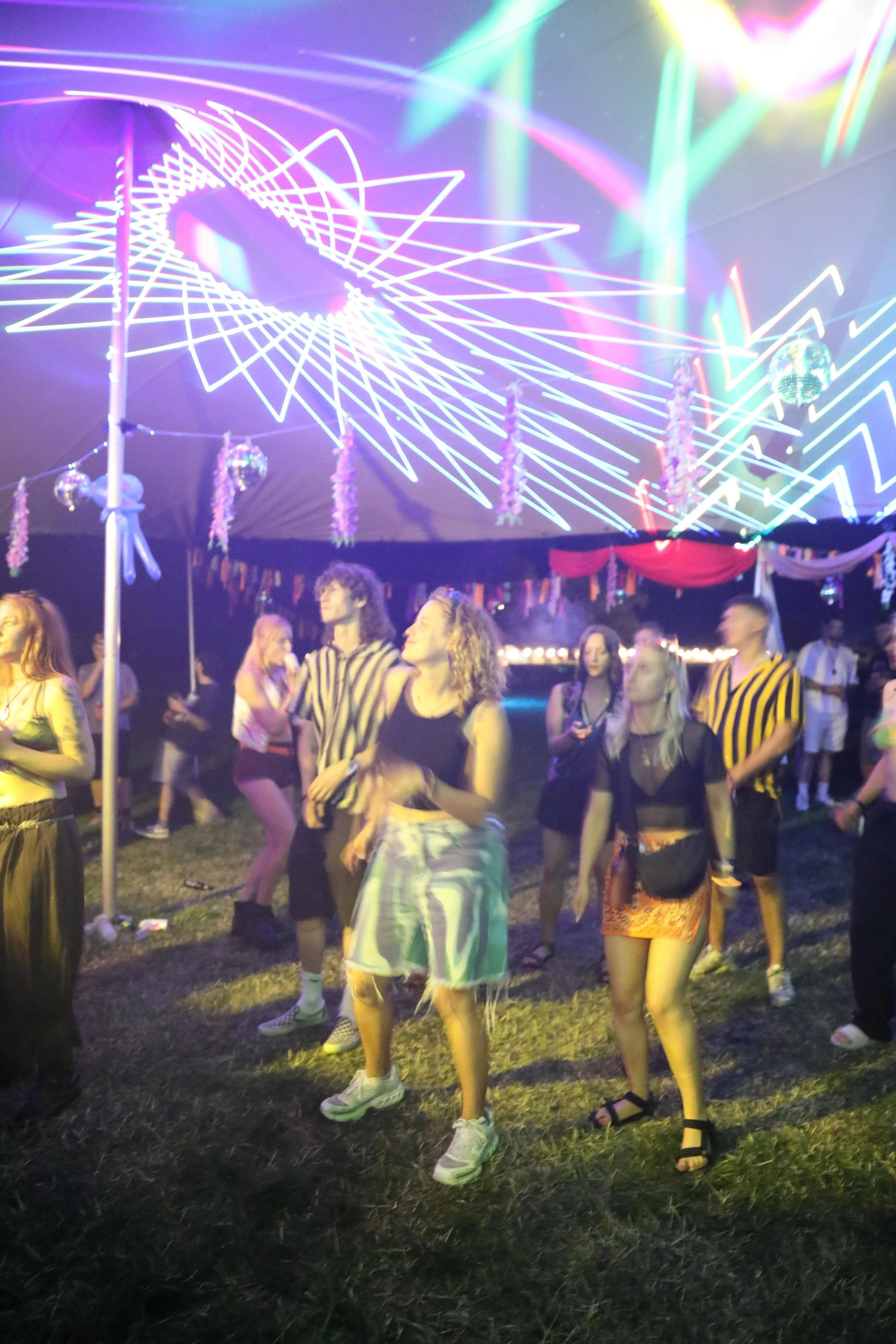 People dancing at a party with colorful neon lights and disco balls hanging from the ceiling.