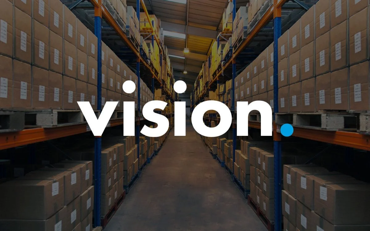 Warehouse aisle with shelves filled with cardboard boxes on both sides, with the word 'vision.' overlaid.