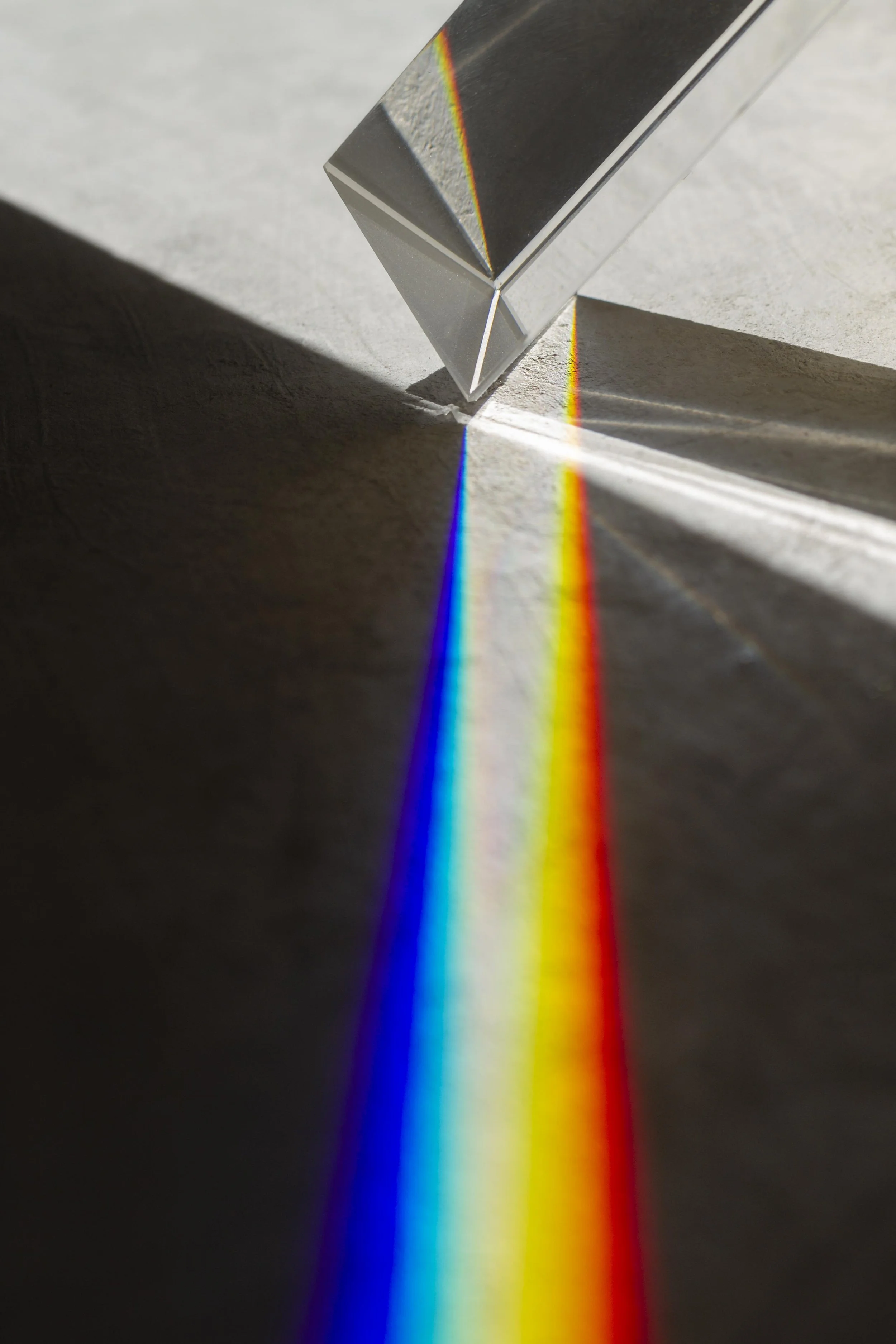 Raio de luz passando por um prisma de vidro, criando um espectro de cores no chão.