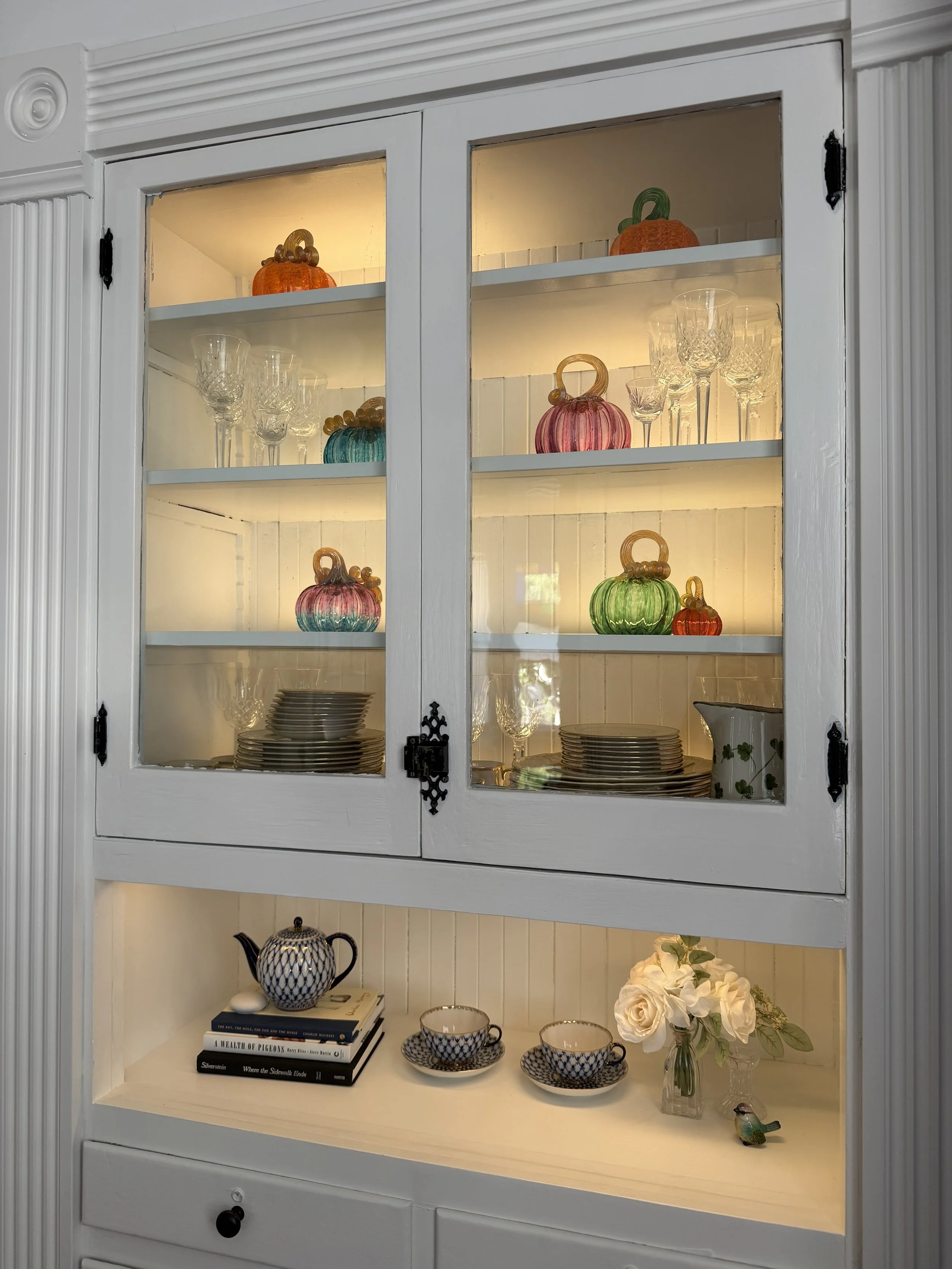 Built-in dining room hutch lit from within and decorated with colorful glass pumpkins for fall