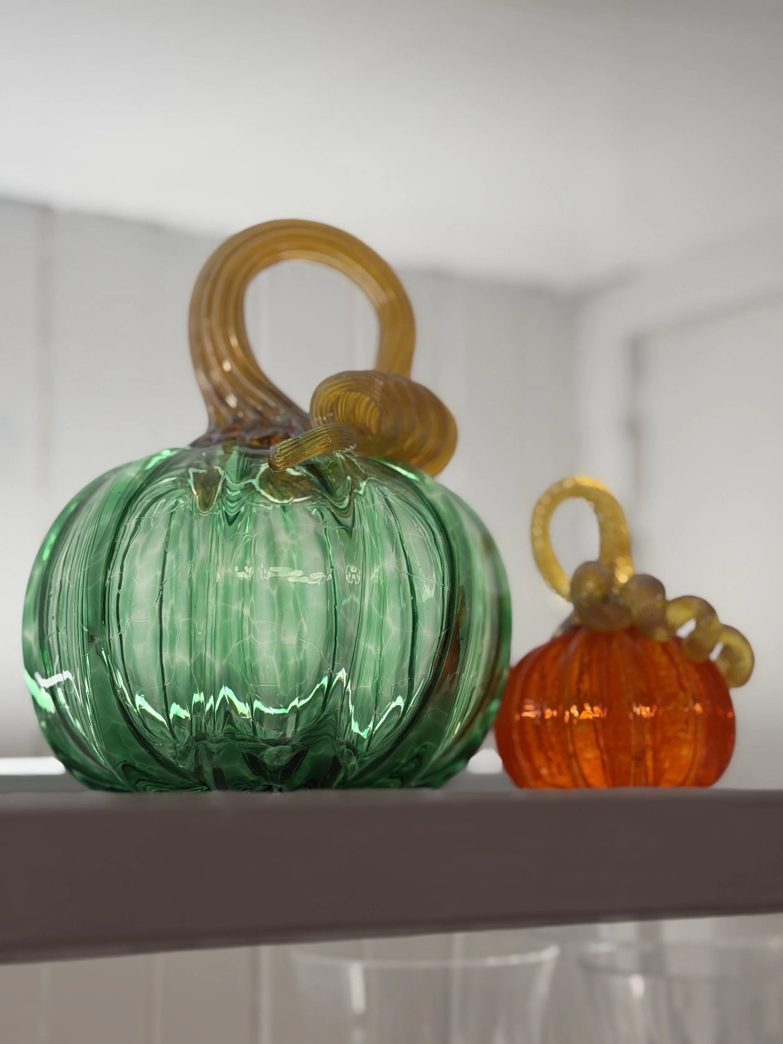 Green and orange hand-blown glass pumpkins displayed together on a dining room hutch shelf