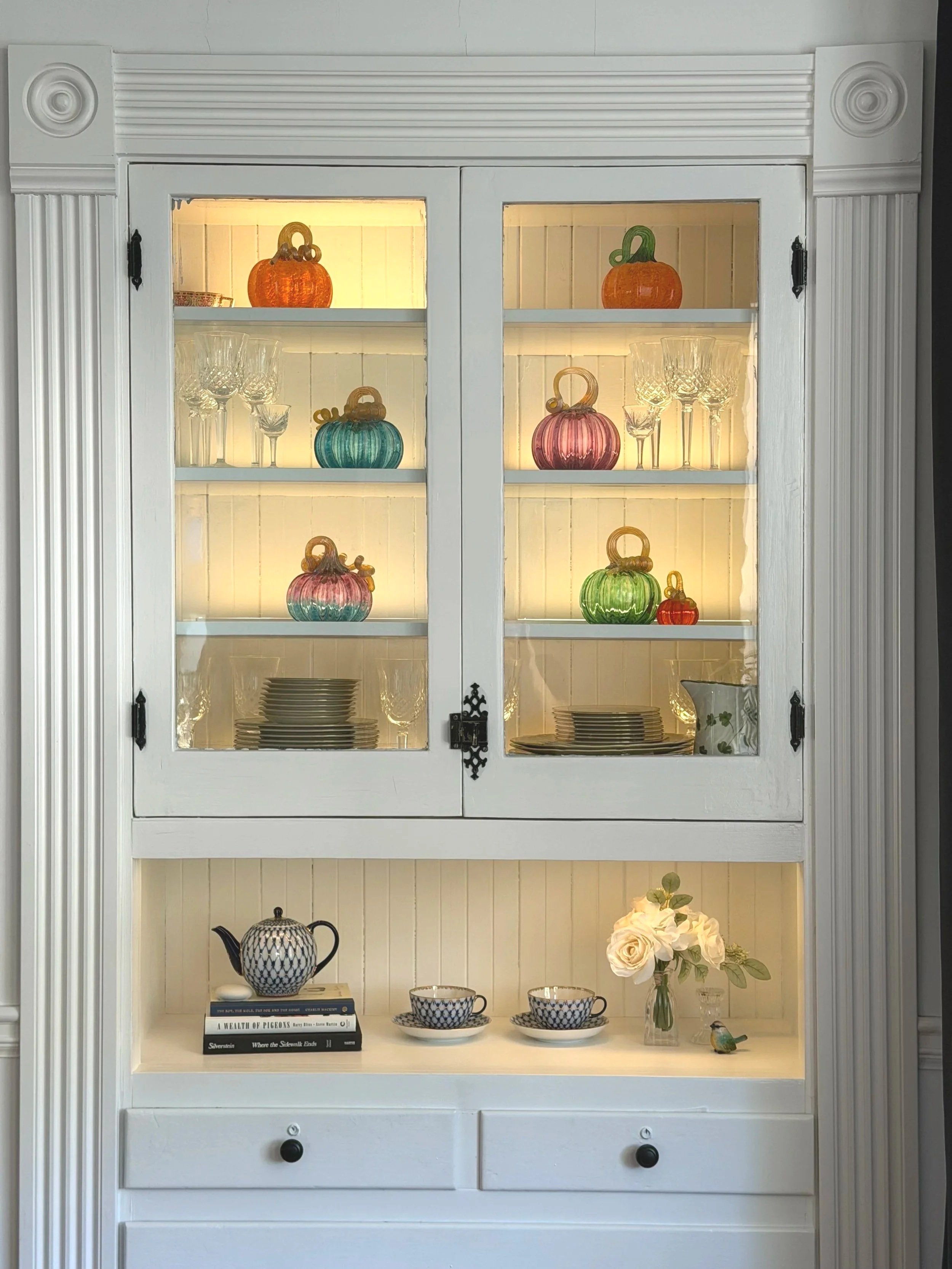 Original 1900 built-in dining room hutch lit and decorated with colorful glass pumpkins for fall