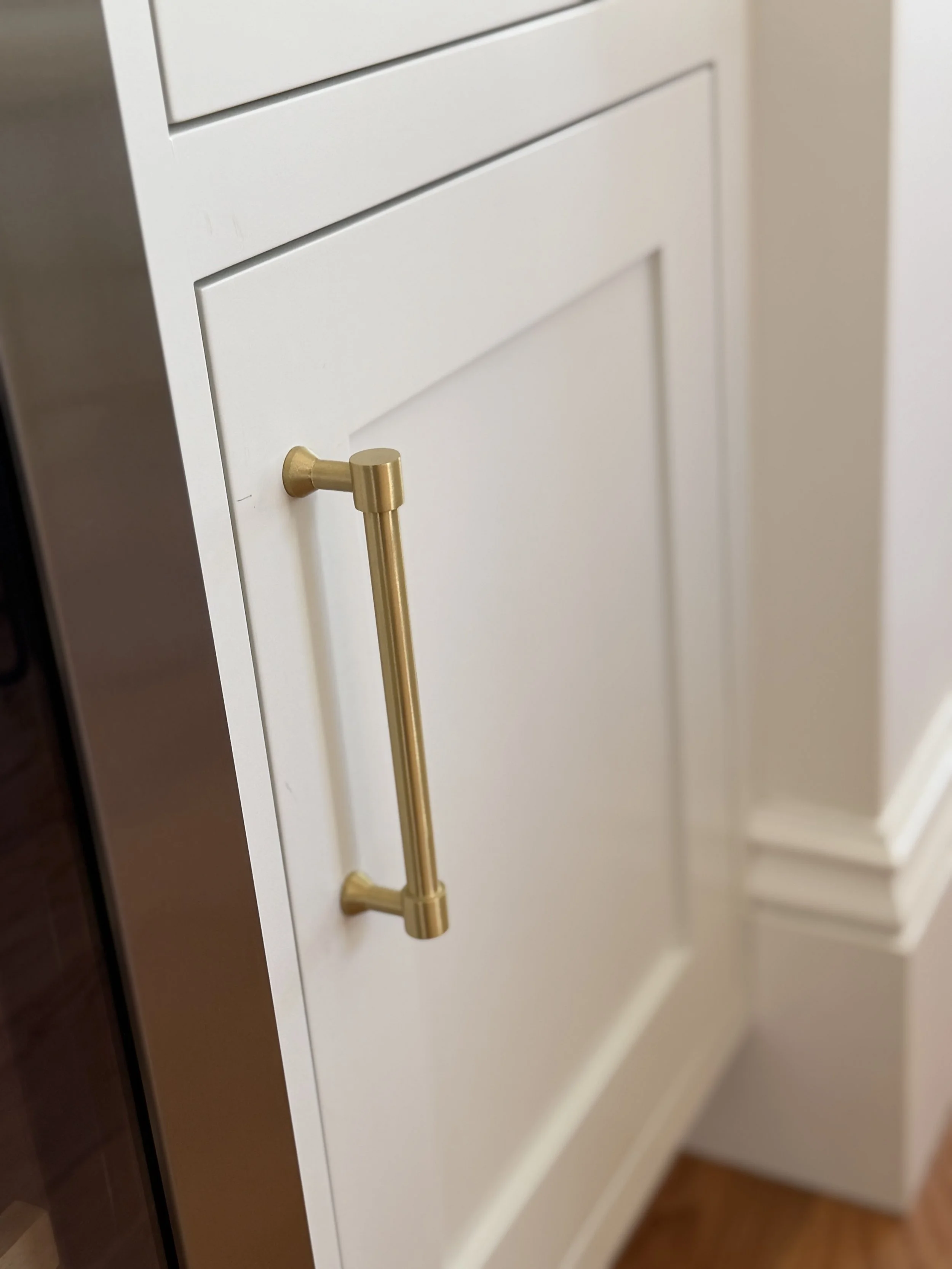 Detail of white inset cabinetry with a recessed panel door and brass hardware.
