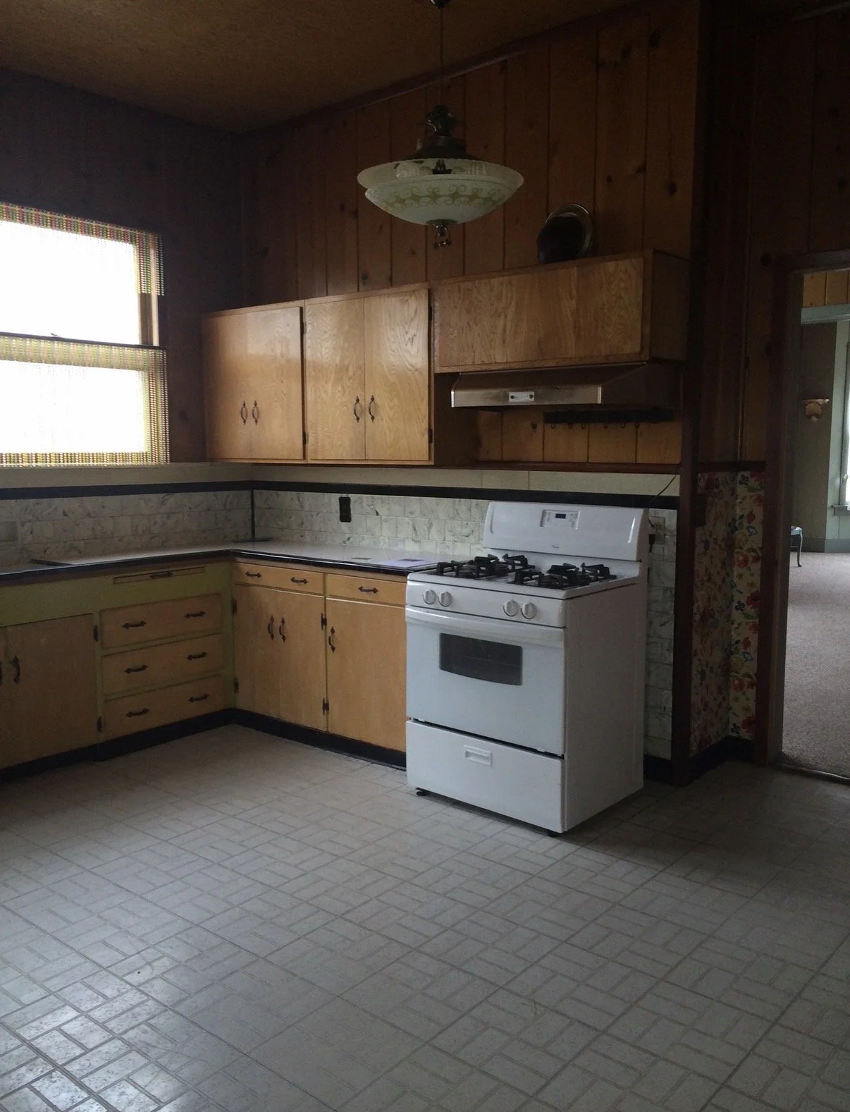 kitchen as it looked when we bought our 1900 house, with wood-paneled walls, wood cabinetry and a small white range, before the renovation.