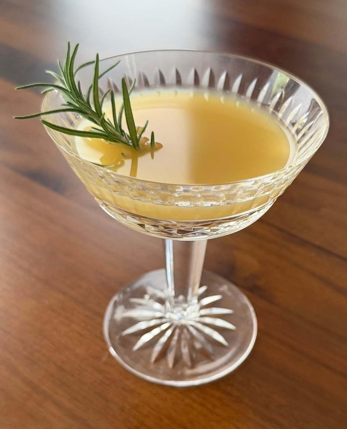 Golden pear mocktail in a Waterford cut-crystal coupe garnished with fresh rosemary