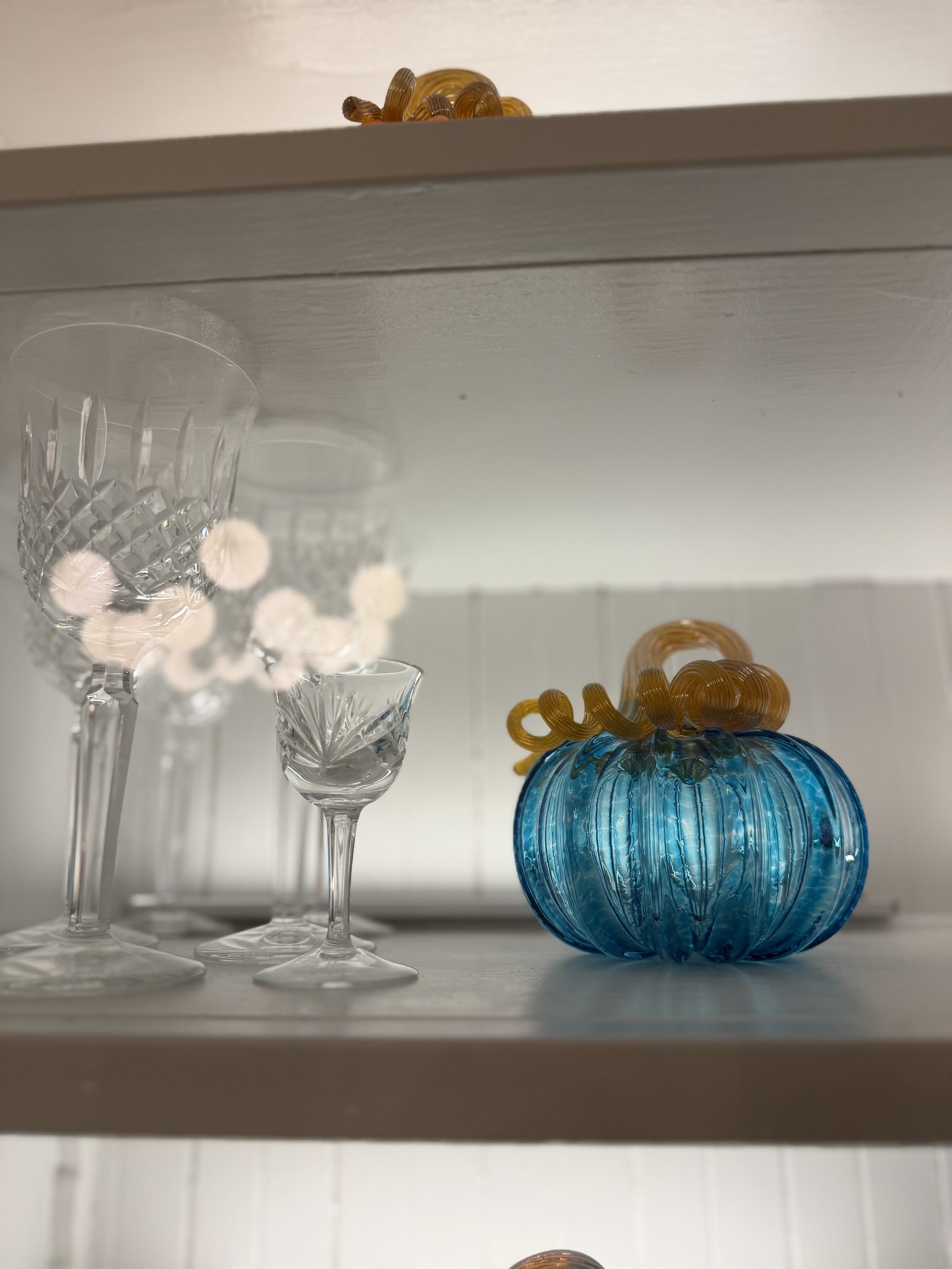 Blue hand-blown glass pumpkin displayed beside crystal glasses in the dining room hutch