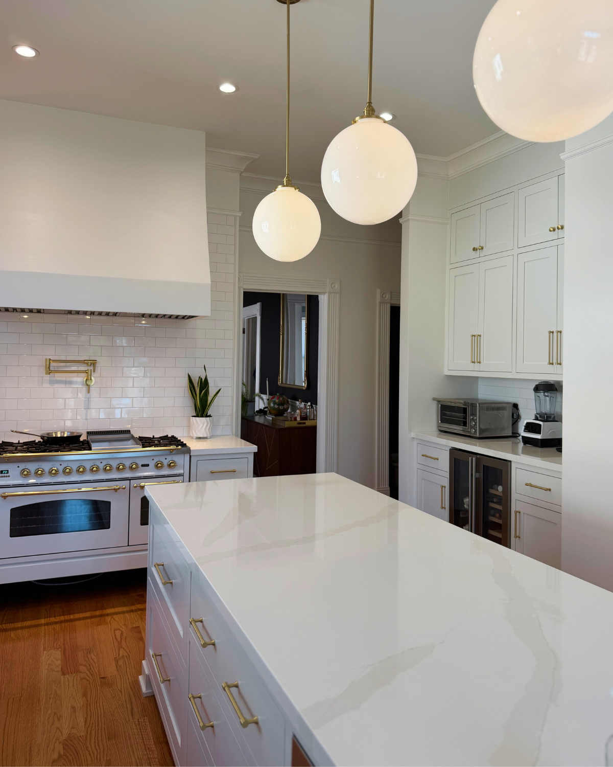 White kitchen in a 1900 house with tall cabinetry, a large island, globe pendant lights, a white range and built-out range hood.