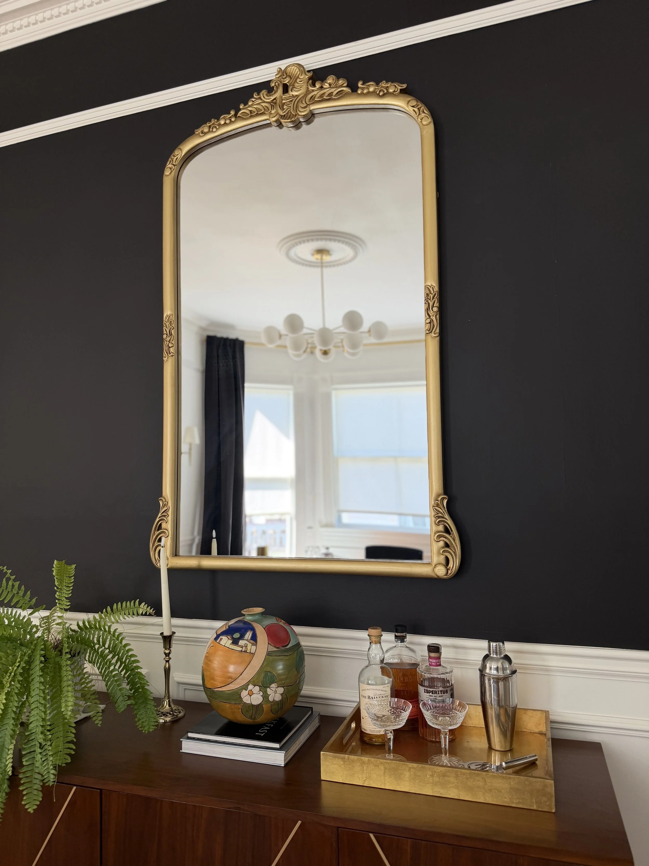 Large antique-inspired gold mirror hanging on black dining room wall