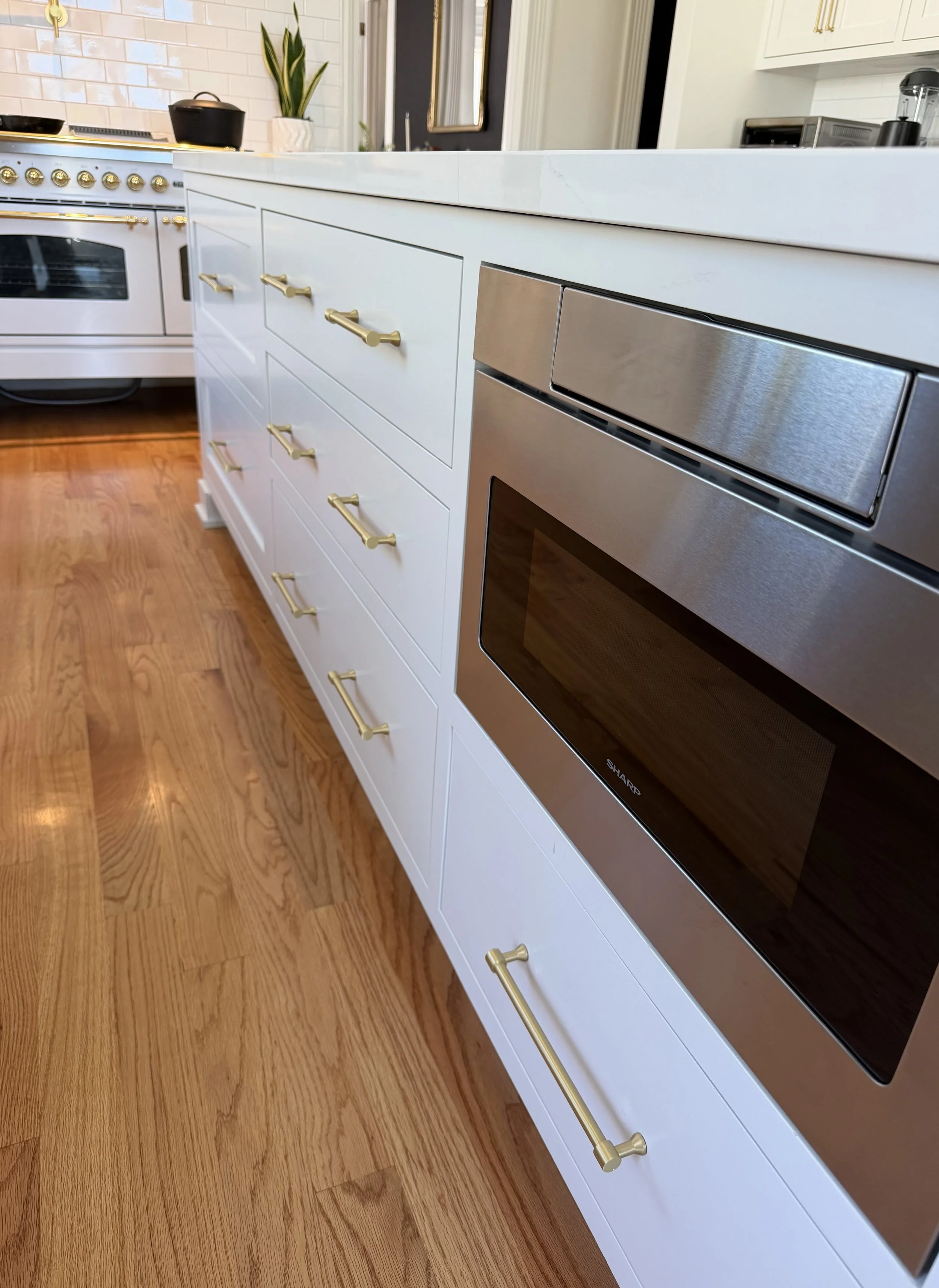 Large white kitchen island with inset drawers, brass hardware and a microwave integrated into the cabinetry.