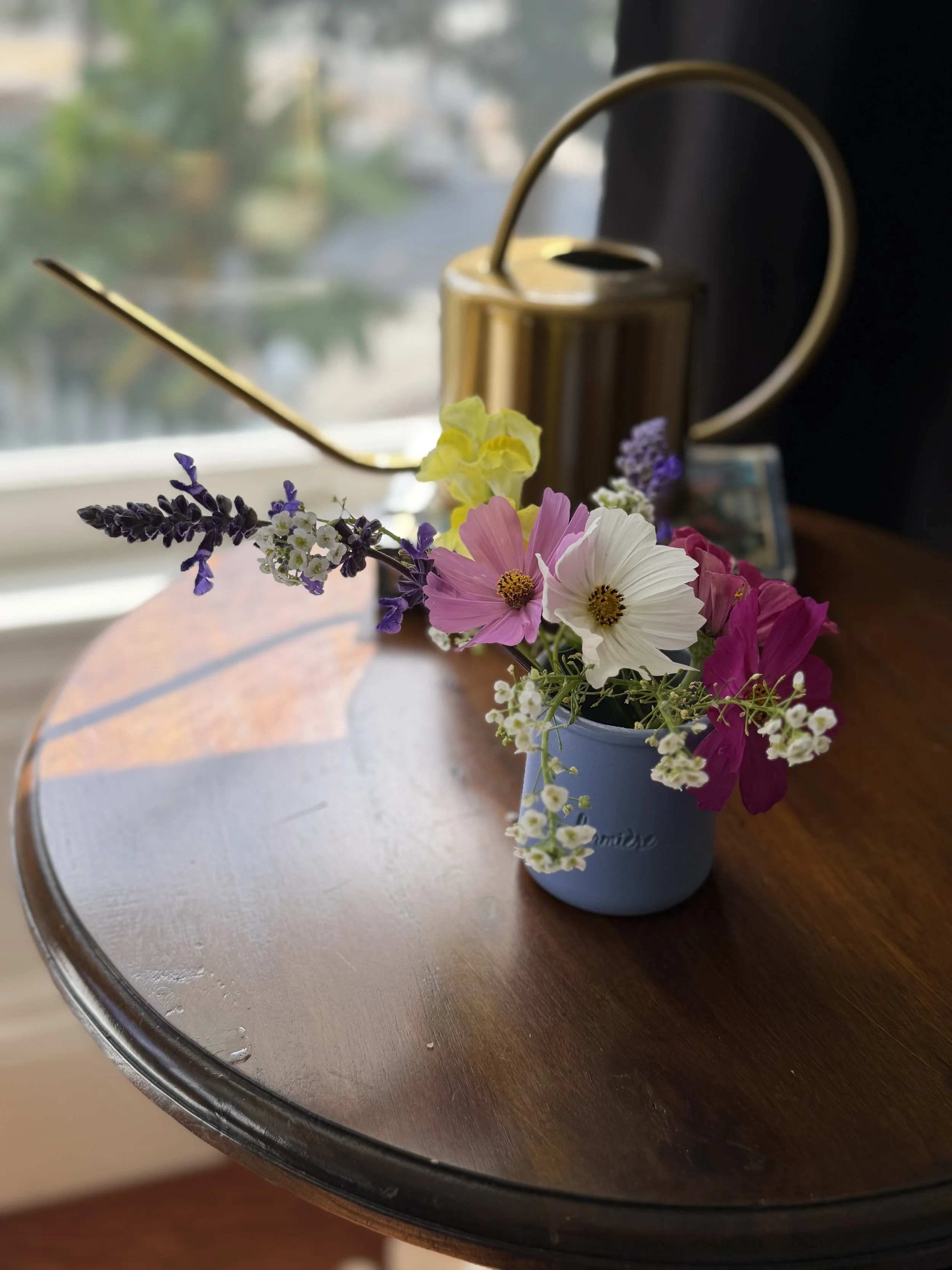 September garden flowers arranged in a small blue jar beside a brass watering can