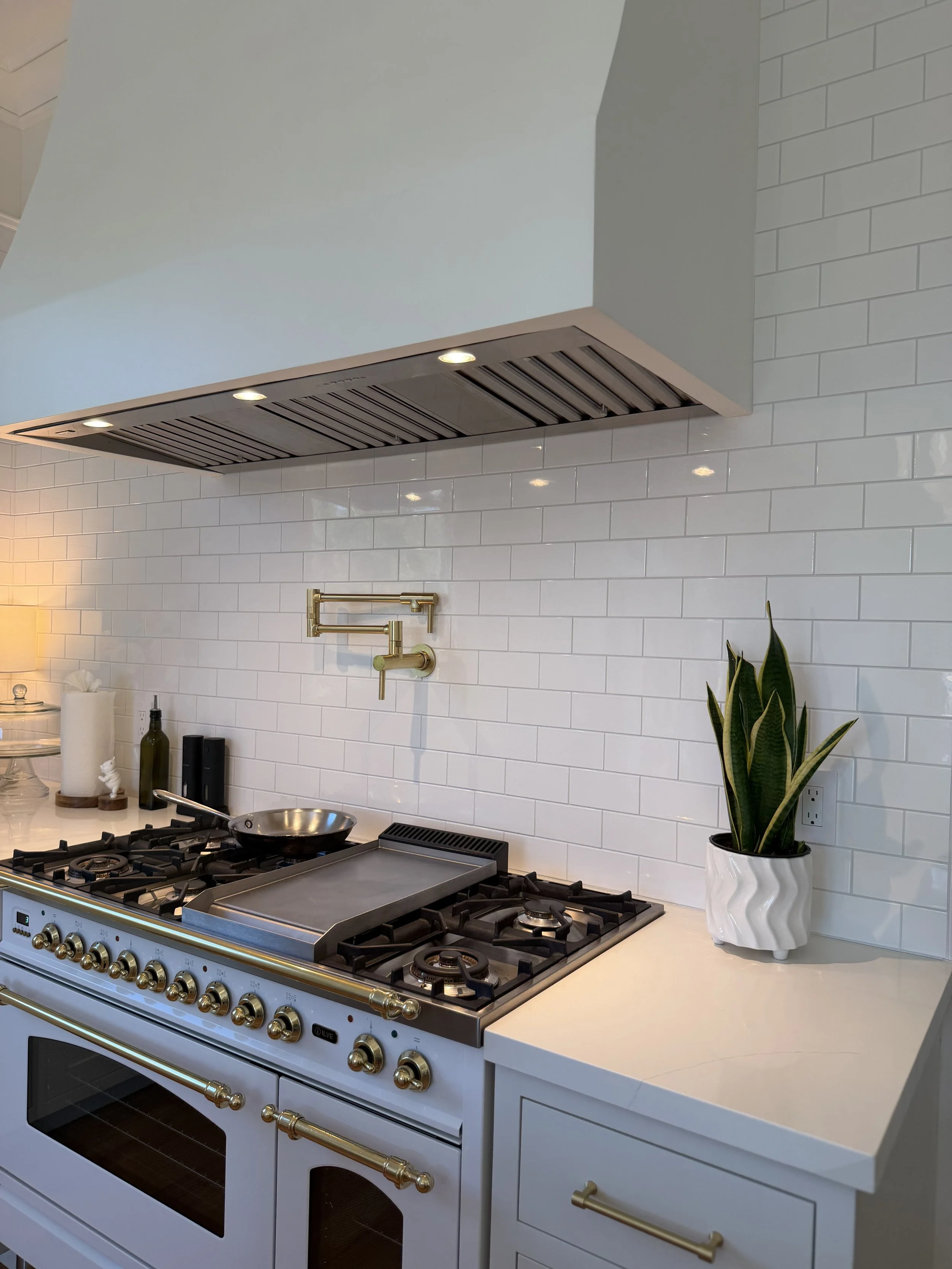 Large white range beneath a built-out range hood with white subway tile and a brass pot filler in a renovated 1900 kitchen.