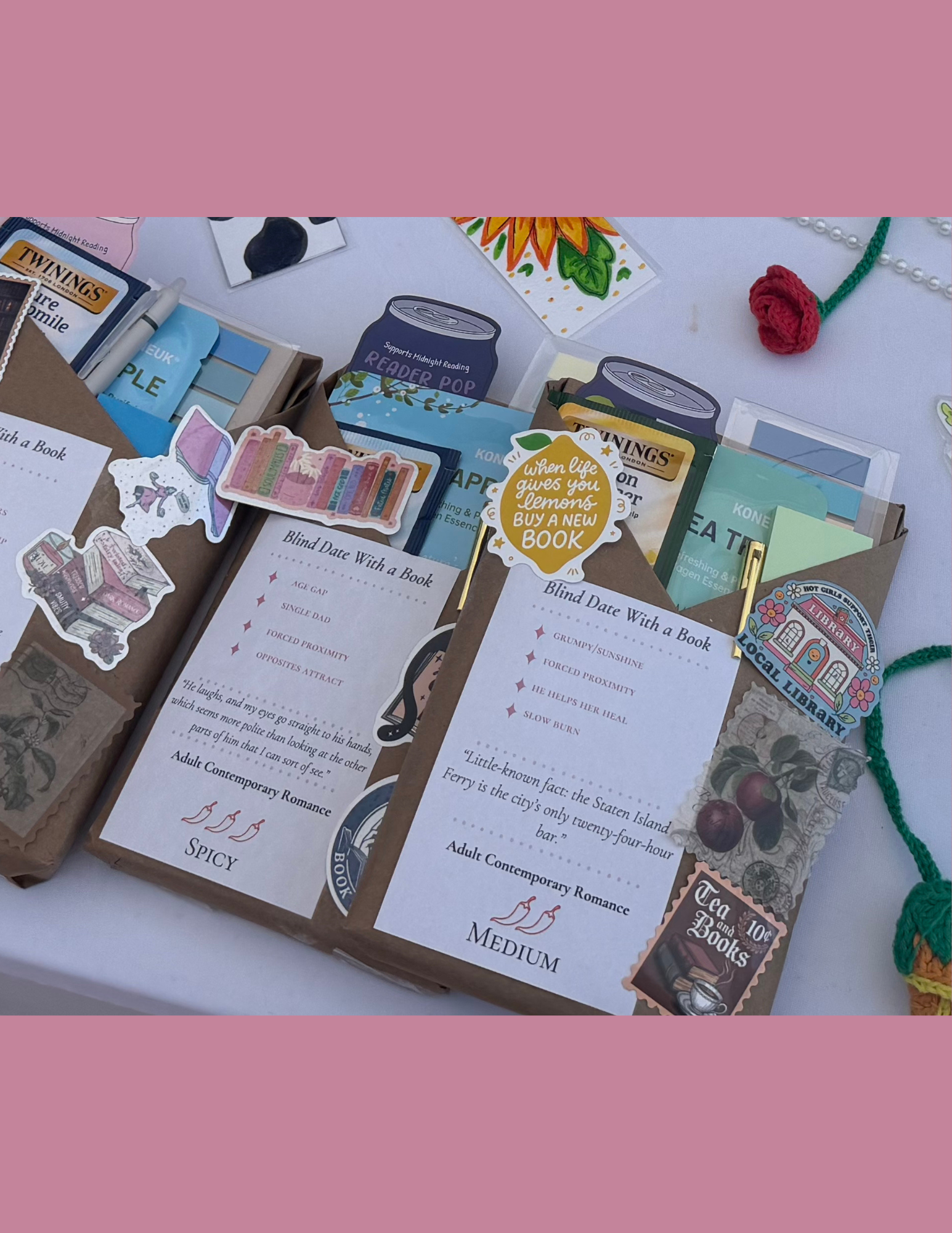 Decorative display with paper book-themed items, stickers, and informational cards arranged on a white surface, including a sunflower, a red yarn flower, and a painted decorative item.